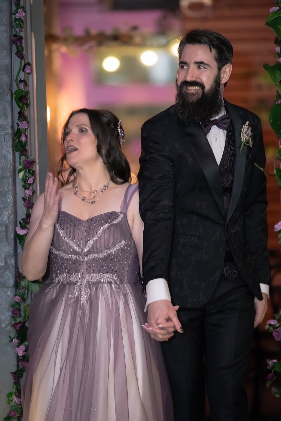 Bride in lavender gown and groom in black suit share a candid moment during their wedding reception.
