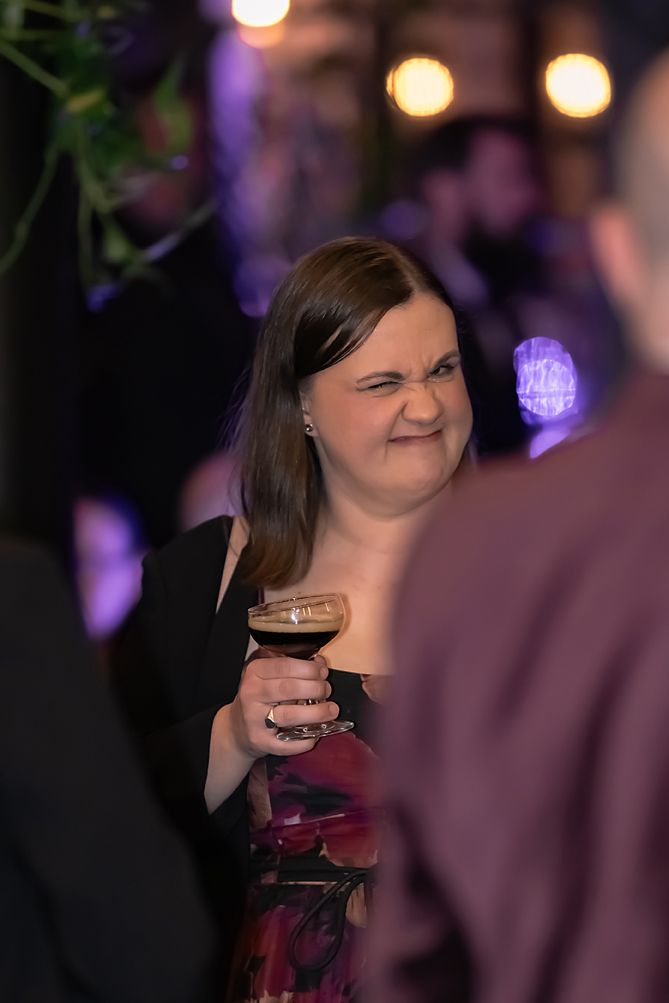 People enjoying drinks and conversation at a dimly lit social gathering with purple lighting.