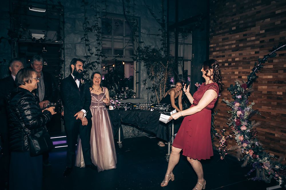 A group dances together during a wedding reception in a dimly lit rustic venue with brick walls.