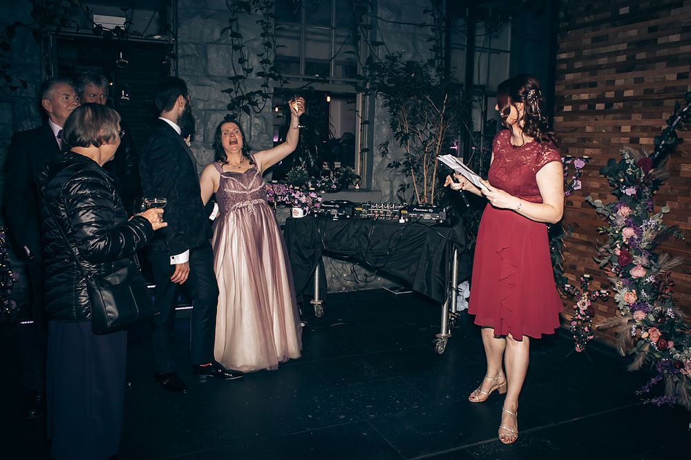 People dancing together at a reception in a dimly lit event space with decorative lighting and rustic decor.