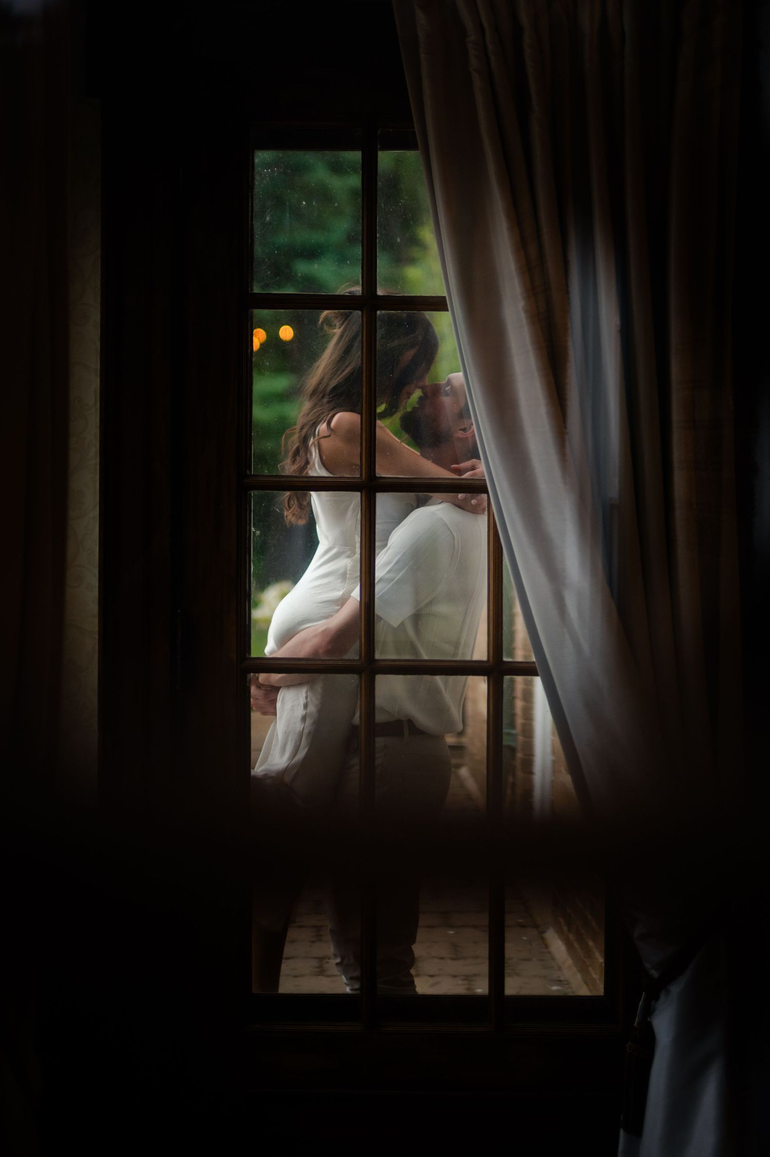 A couple in white outfits walks and dances together in a romantic garden setting during a sunny day.