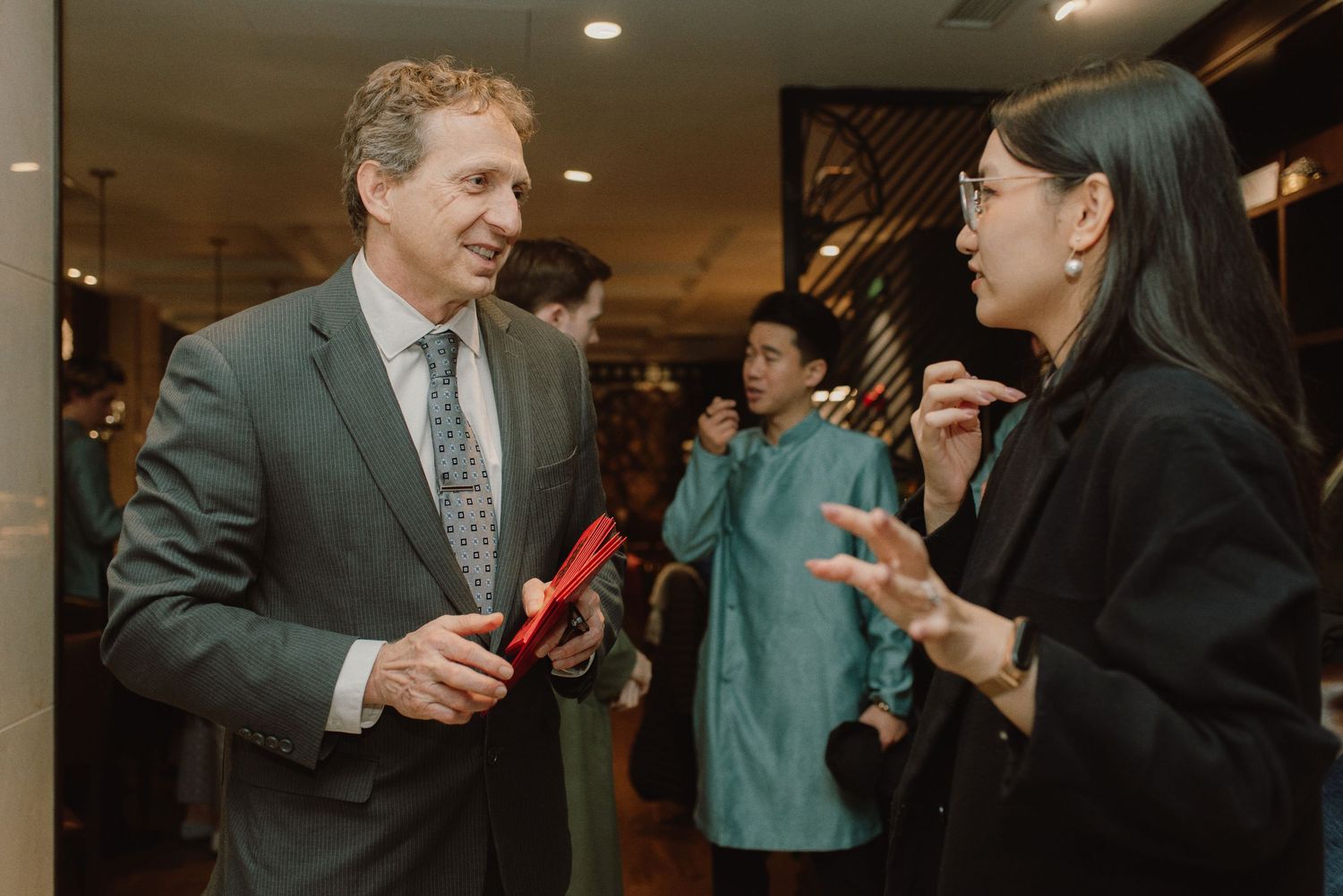 People in formal attire holding red gift boxes during a celebration.