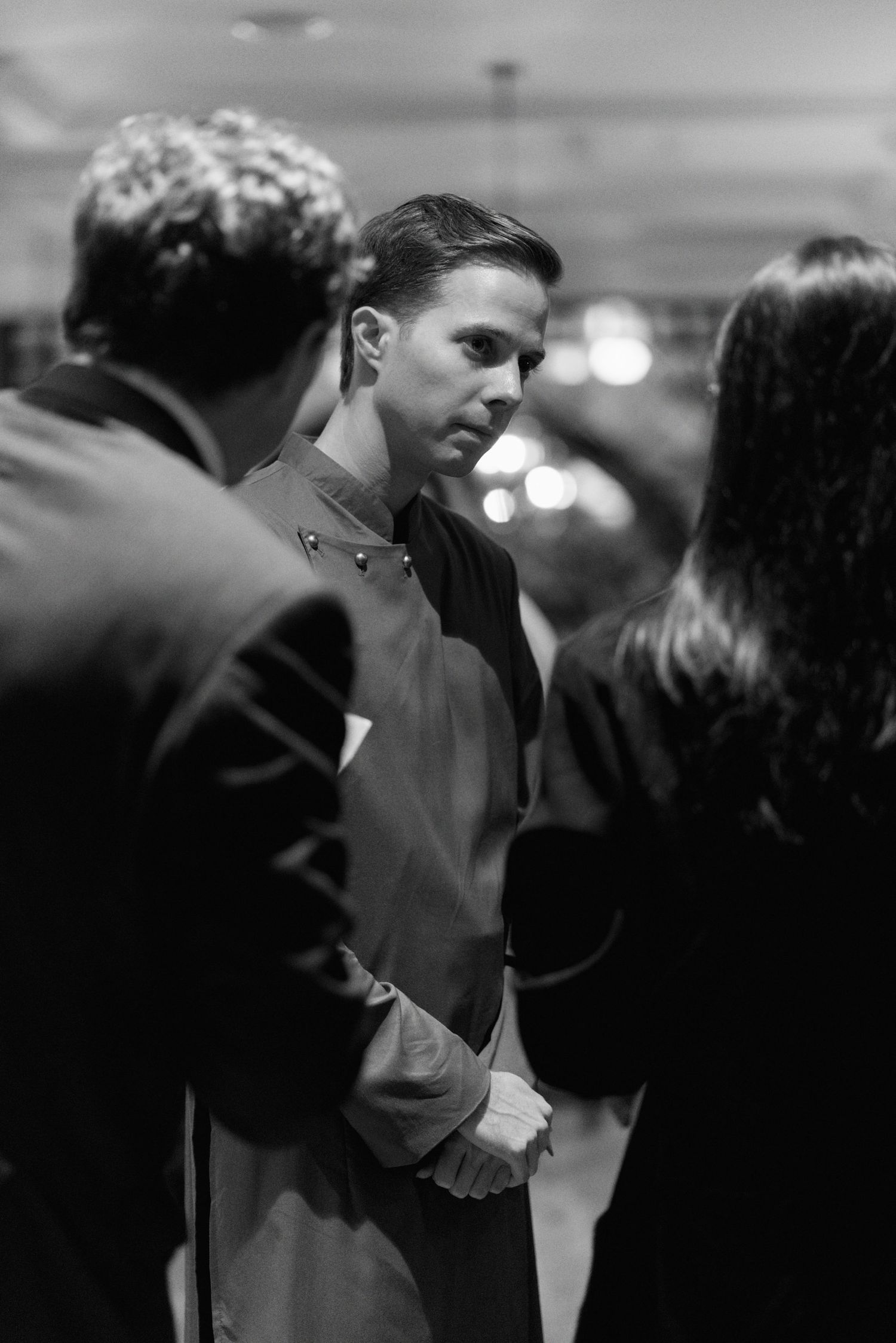 A black and white scene shows couples dancing and embracing at an evening event.
