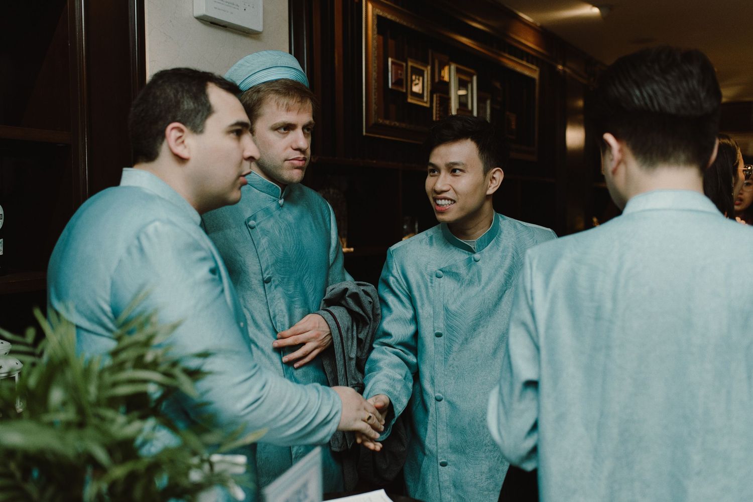 People in coordinated blue and green outfits gather in a dimly lit indoor space.