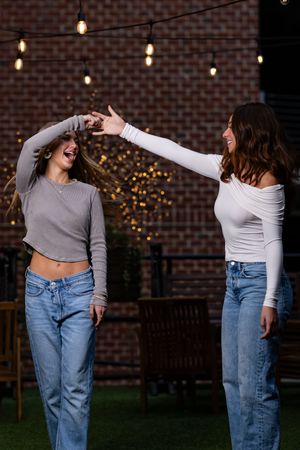 Four candid dance movement poses showing a person in jeans and a cropped top against a brick wall with string lights.