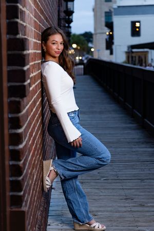 Fashion photo series showing casual outfit with jeans and white top posed against brick wall on wooden boardwalk at dusk.