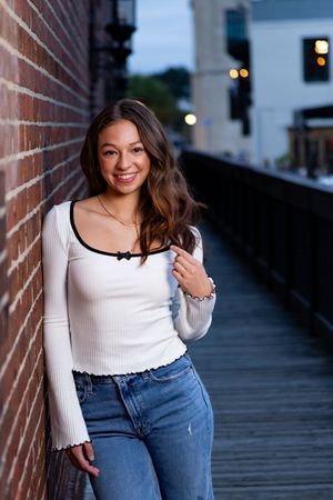 Woman in white long sleeve top and jeans poses on wooden boardwalk at sunset.