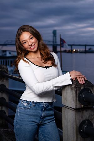 Casual waterfront portraits at dusk featuring a white sweater and jeans against a harbor backdrop.