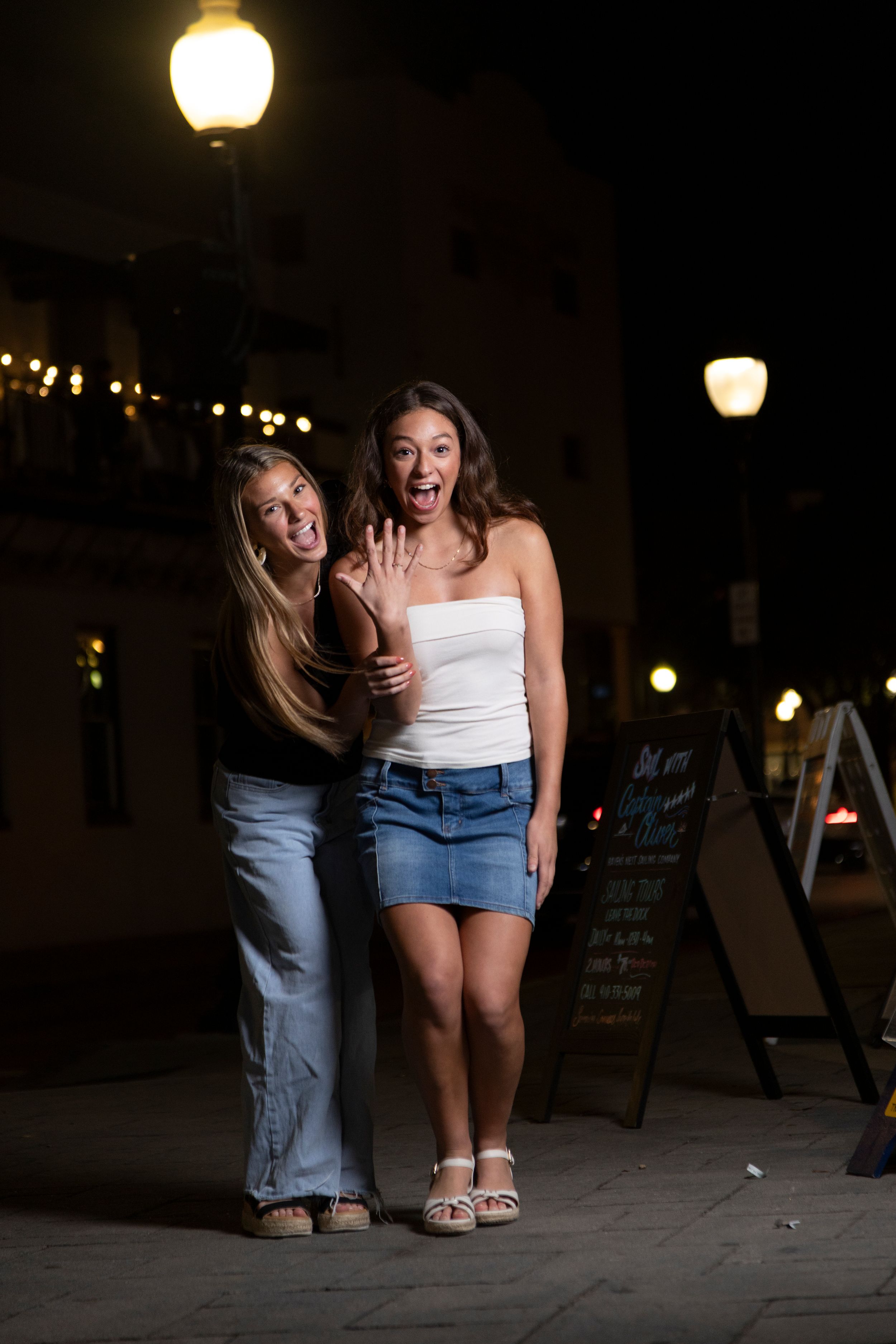 Two friends laugh together at night on a street lit by glowing lanterns and street lamps.