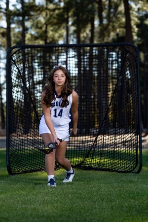 Player crouches in front of lacrosse goal net on grass field during sunny outdoor practice session.