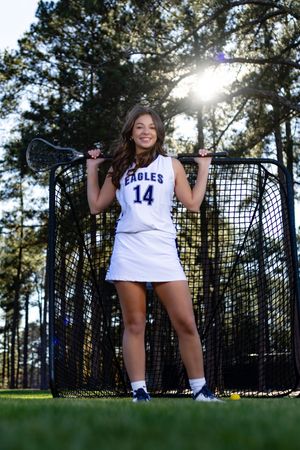 Eagles player number 14 poses with lacrosse stick in front of goal net on sunny field.