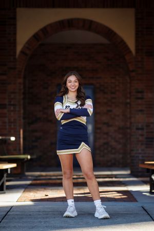 Cheerleader poses confidently in navy blue uniform under a brick archway.