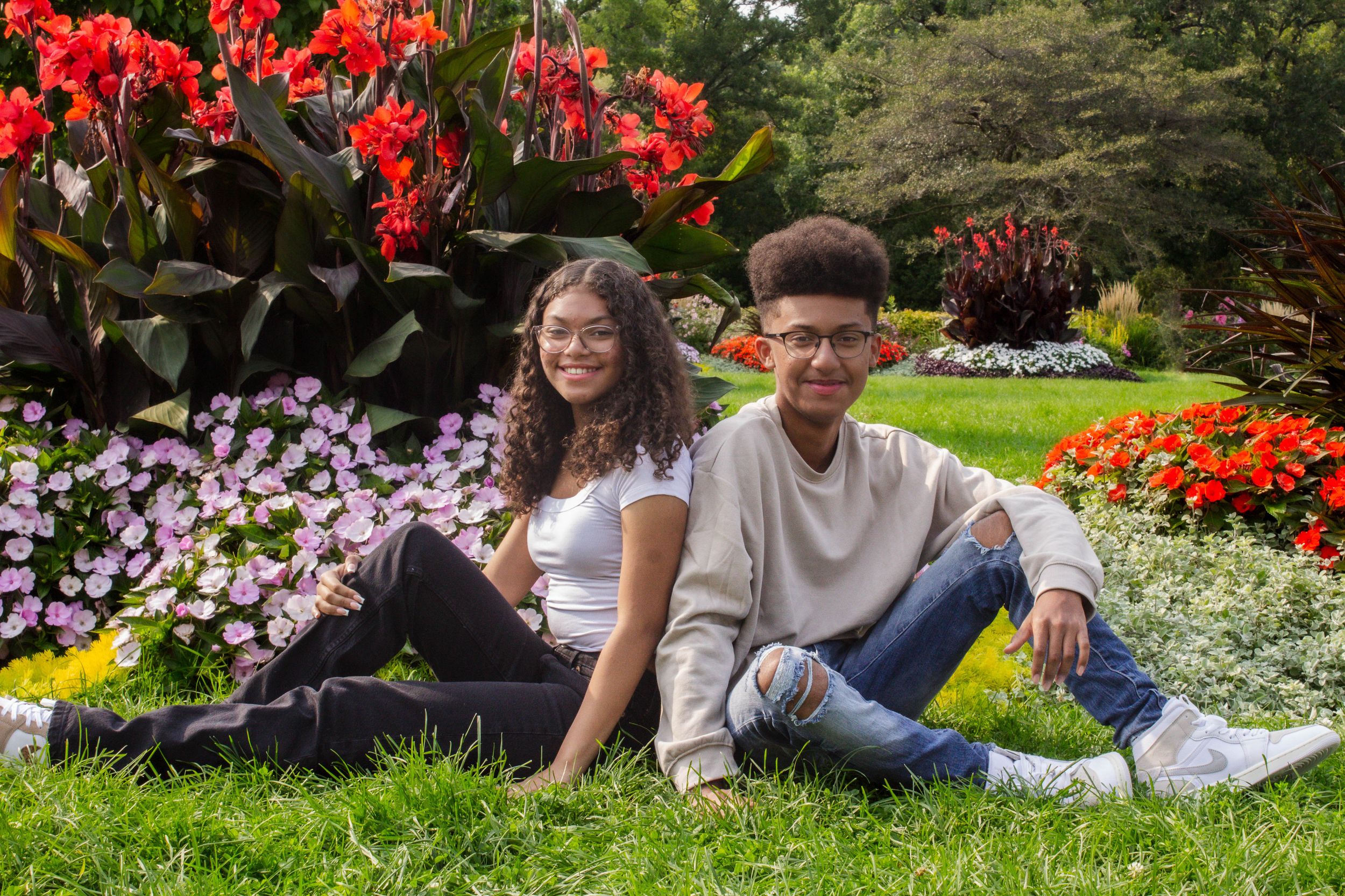 Two young people relaxing in a colorful garden with red cannas, purple petunias and orange marigold flowers.