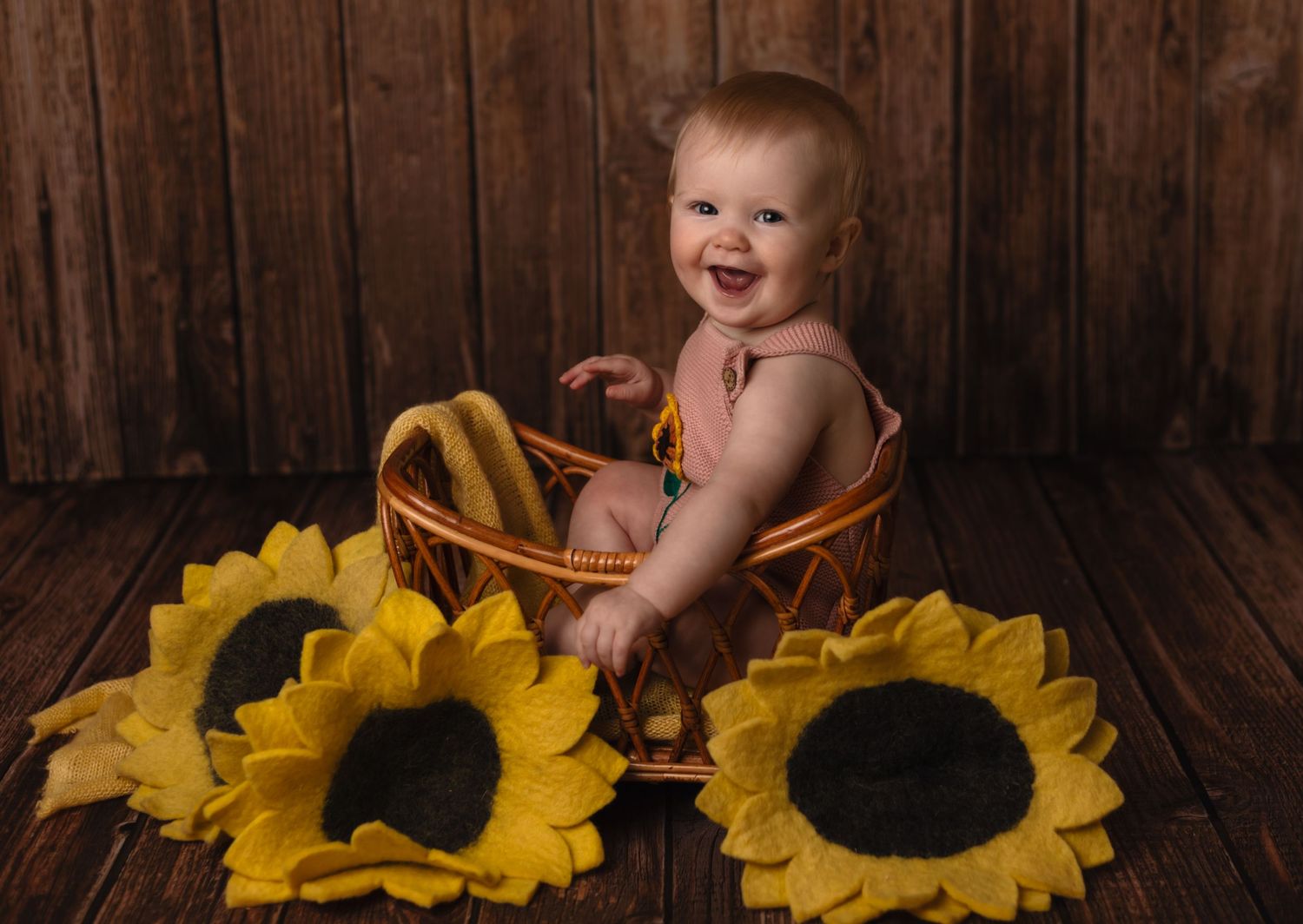 Joyful baby girl sits in a basket surrounded by felt sunflowers at Somerset Portraits studio, a Charlottesville newborn photographer.