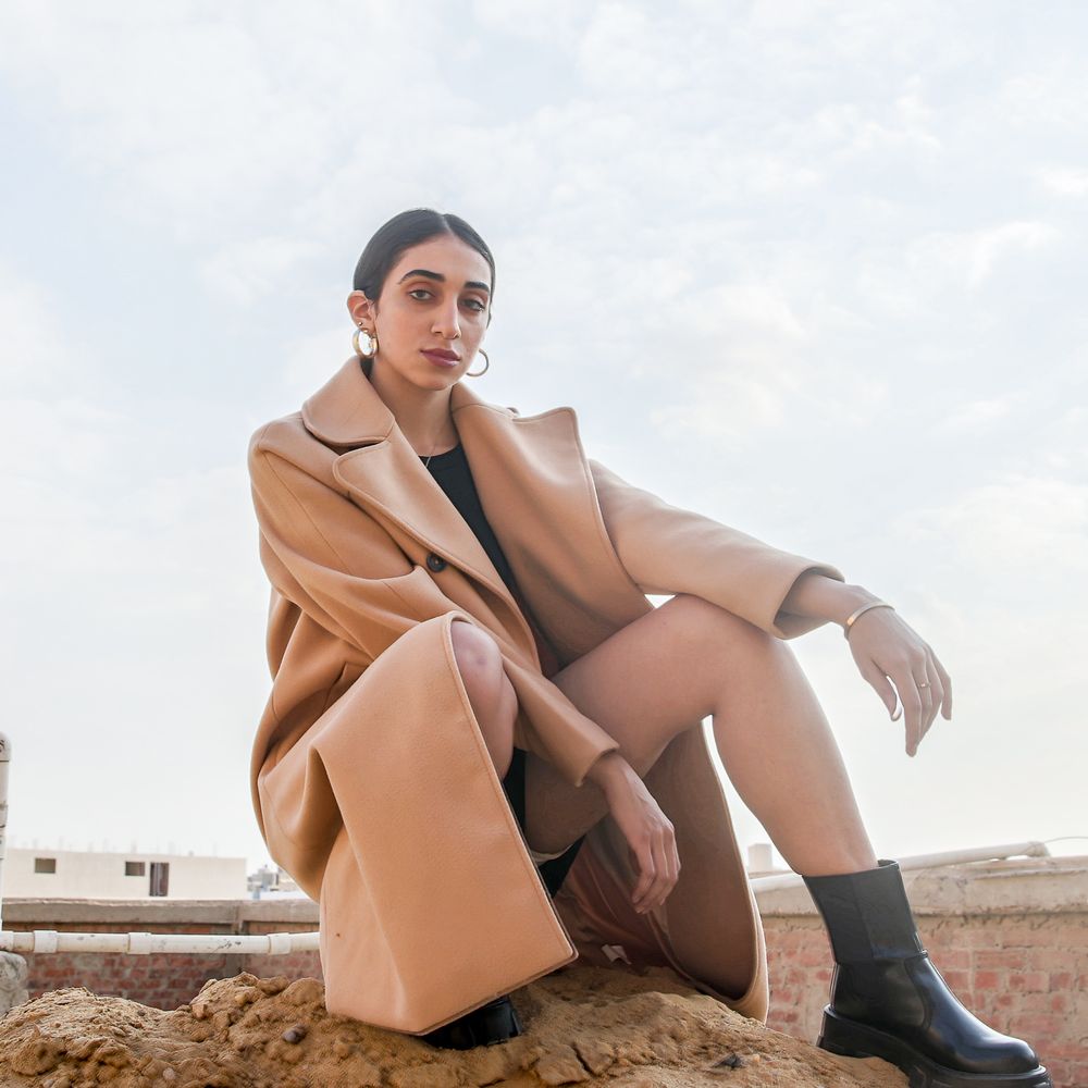 Person in a tan coat and black boots poses in a series of artistic shots against a neutral outdoor backdrop.