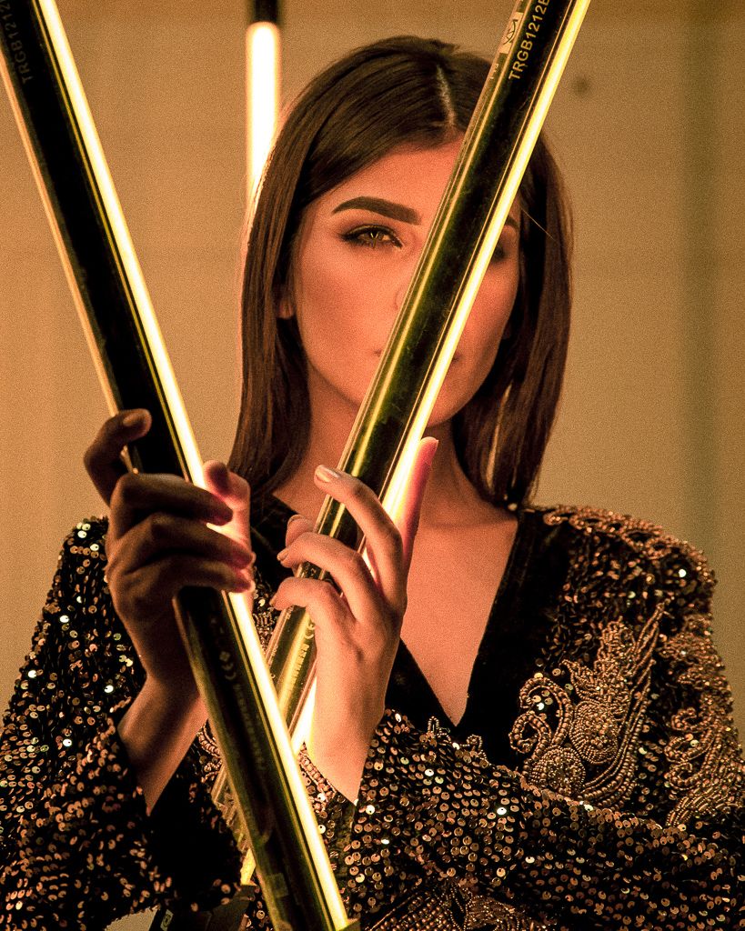 Glamorous fashion shoot with sparkly black sequined outfit and dramatic gold lighting effects.