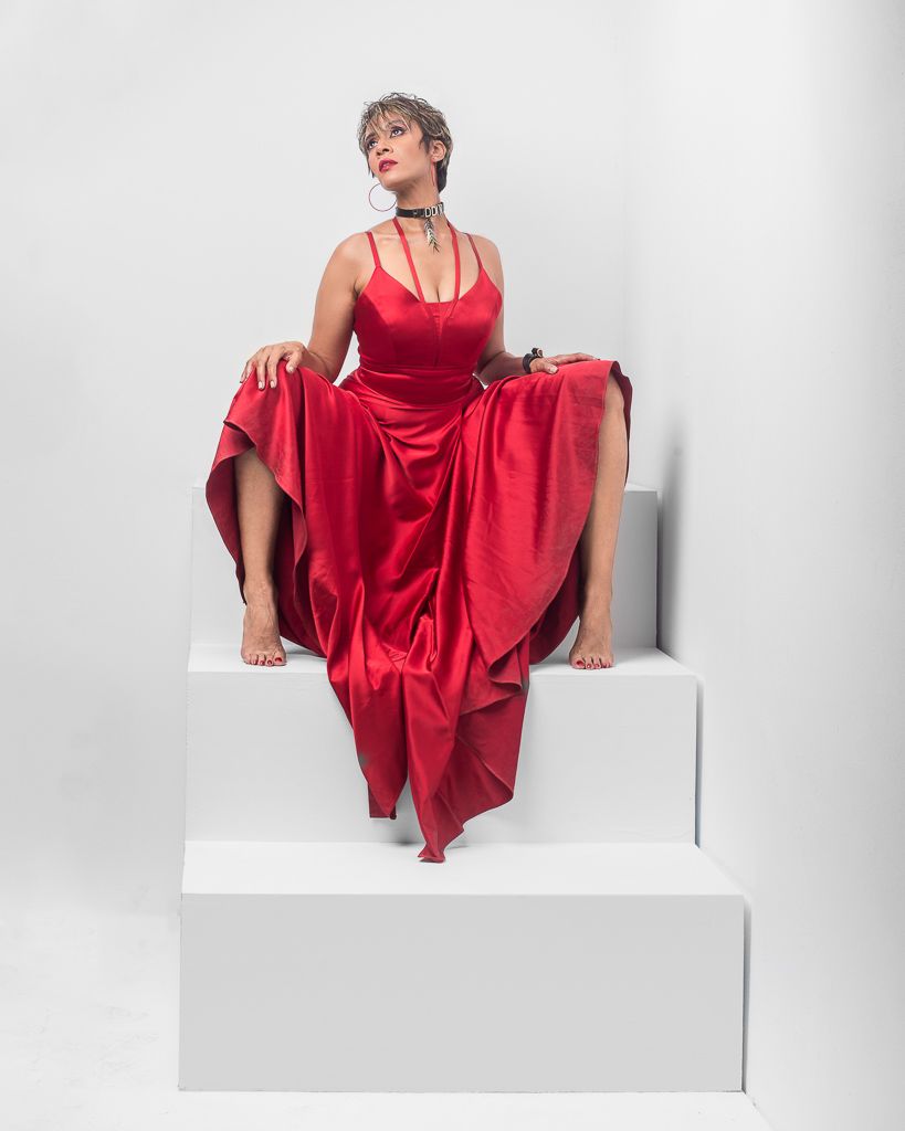 Dynamic fashion poses in a flowing red dress against white backdrop on elevated platform.