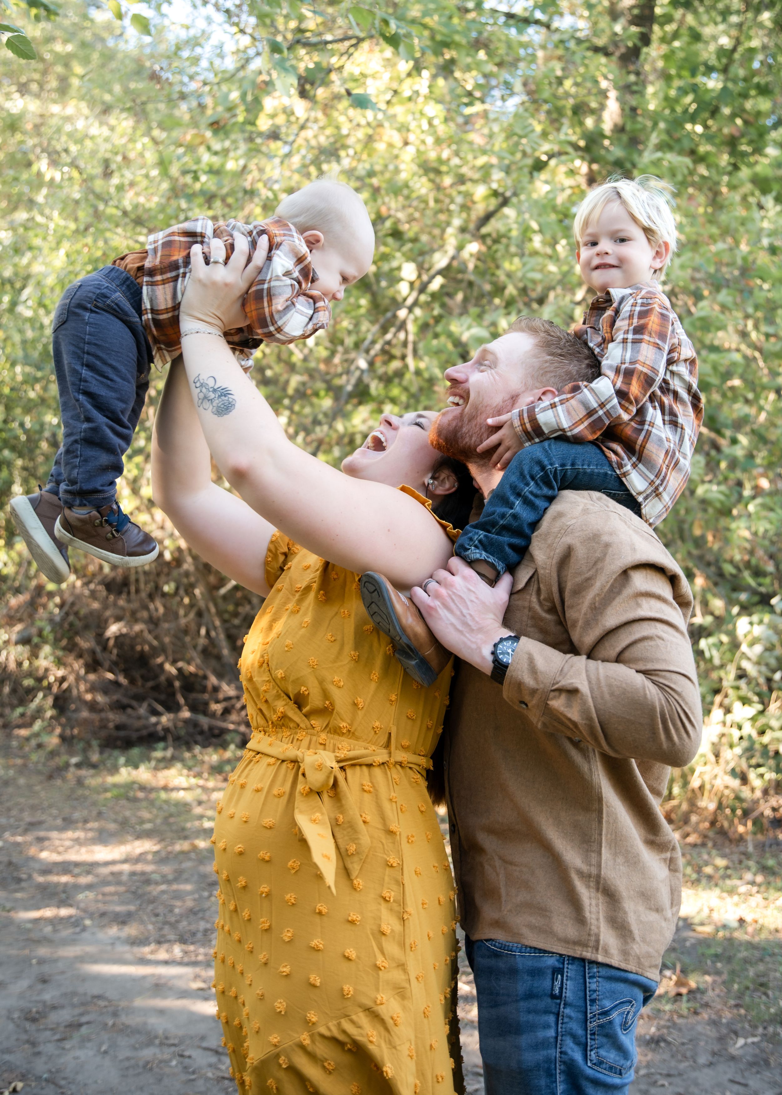 Two people share a tender moment in golden hour lighting while wearing yellow overalls and brown attire in a forest setting.