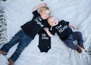Three small children lying on a white blanket wearing matching black shirts with contrasting text.