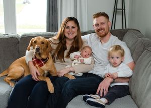 A family relaxes together on a gray couch with their golden retriever wearing a plaid bandana.