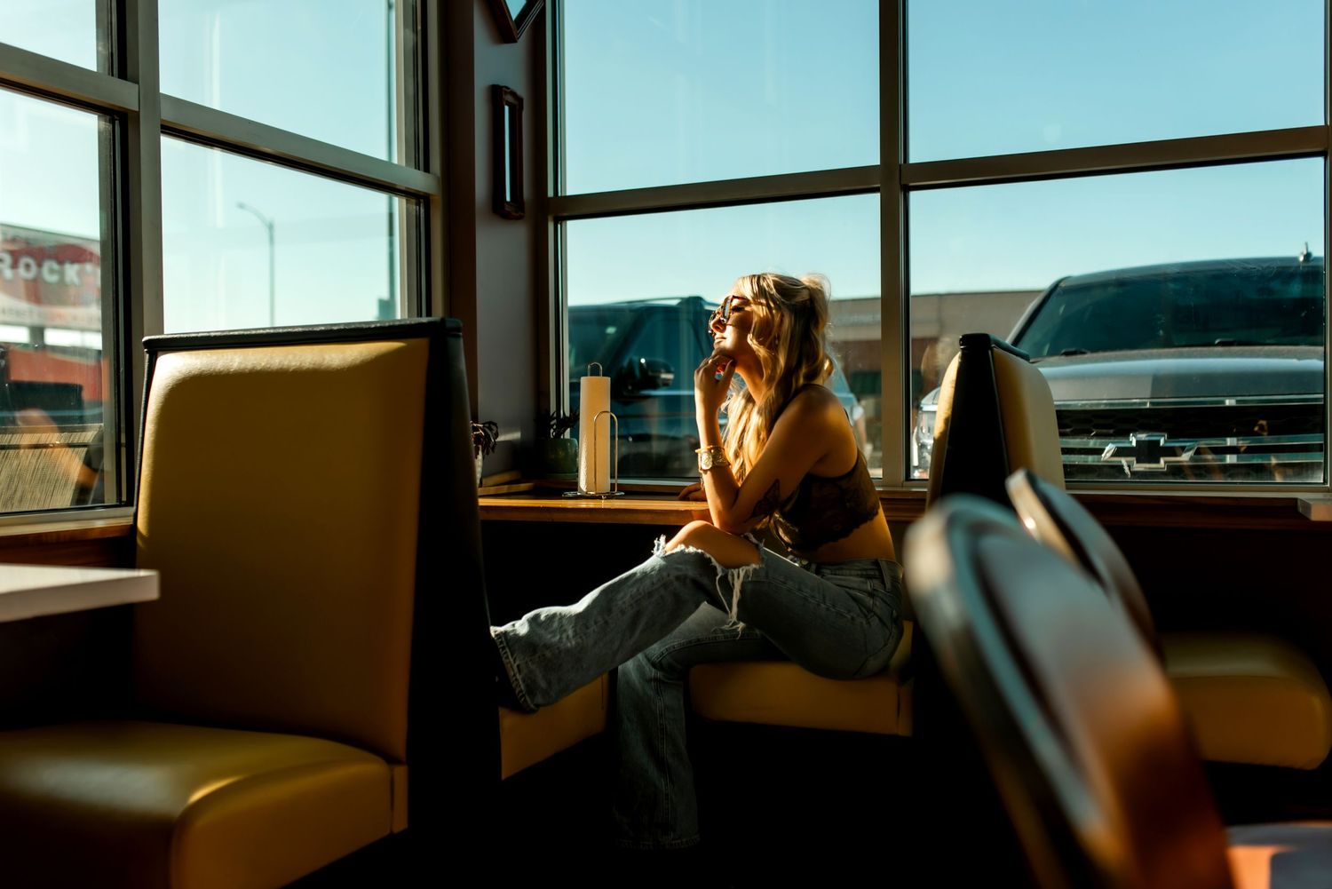 A person sits in an orange booth near large windows in a retro American diner setting during golden hour.