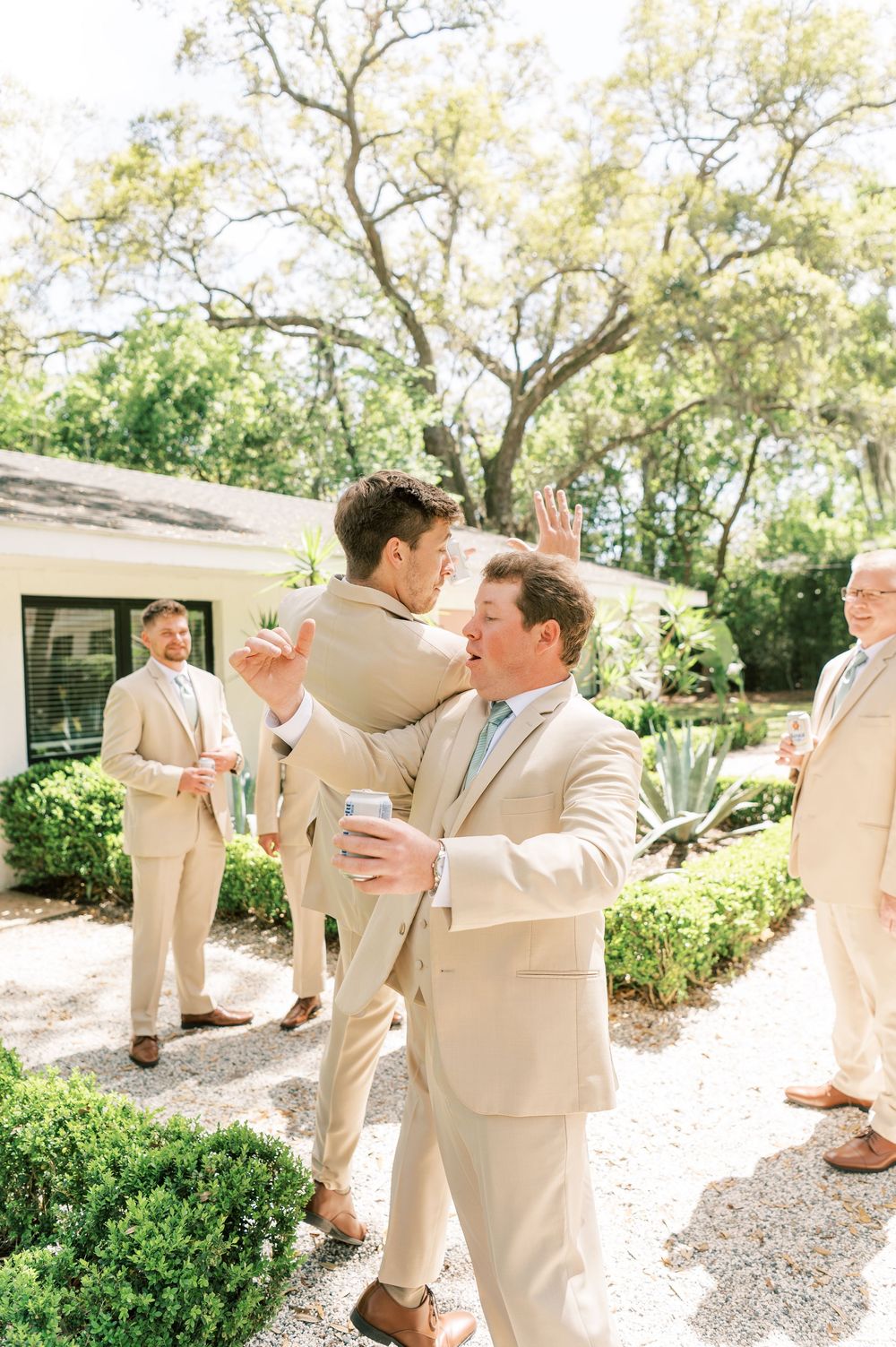 A photo showing groomsmen in tan suits having fun and joking around in a garden setting, photo taken by Fayetteville NC Wedding Photographer