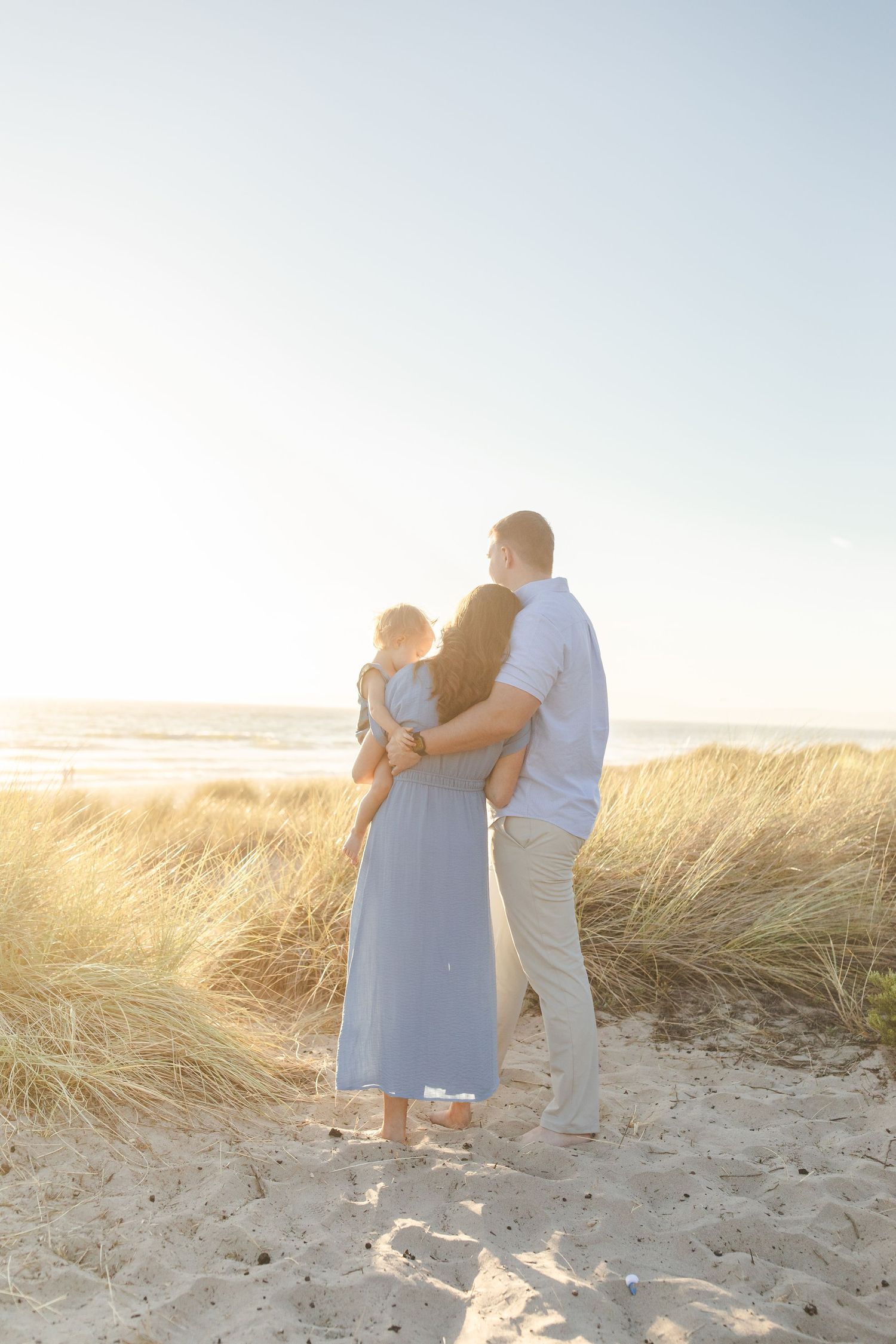 A couple shares an intimate moment walking along sand dunes during golden hour.