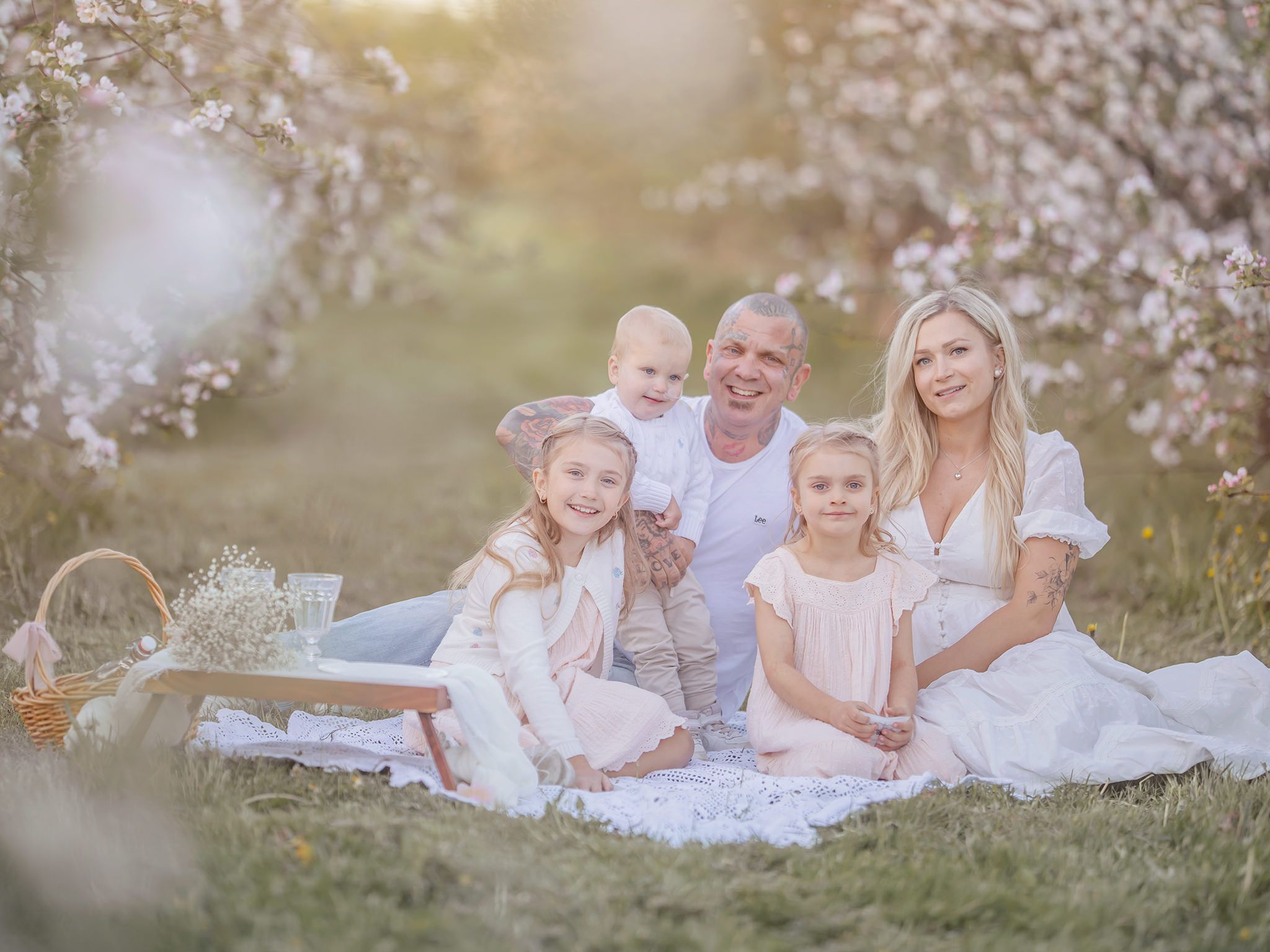 Familj sitter bland blomstrande äppelträd, familjefotografering i Västerås, MemoriesbyM.se