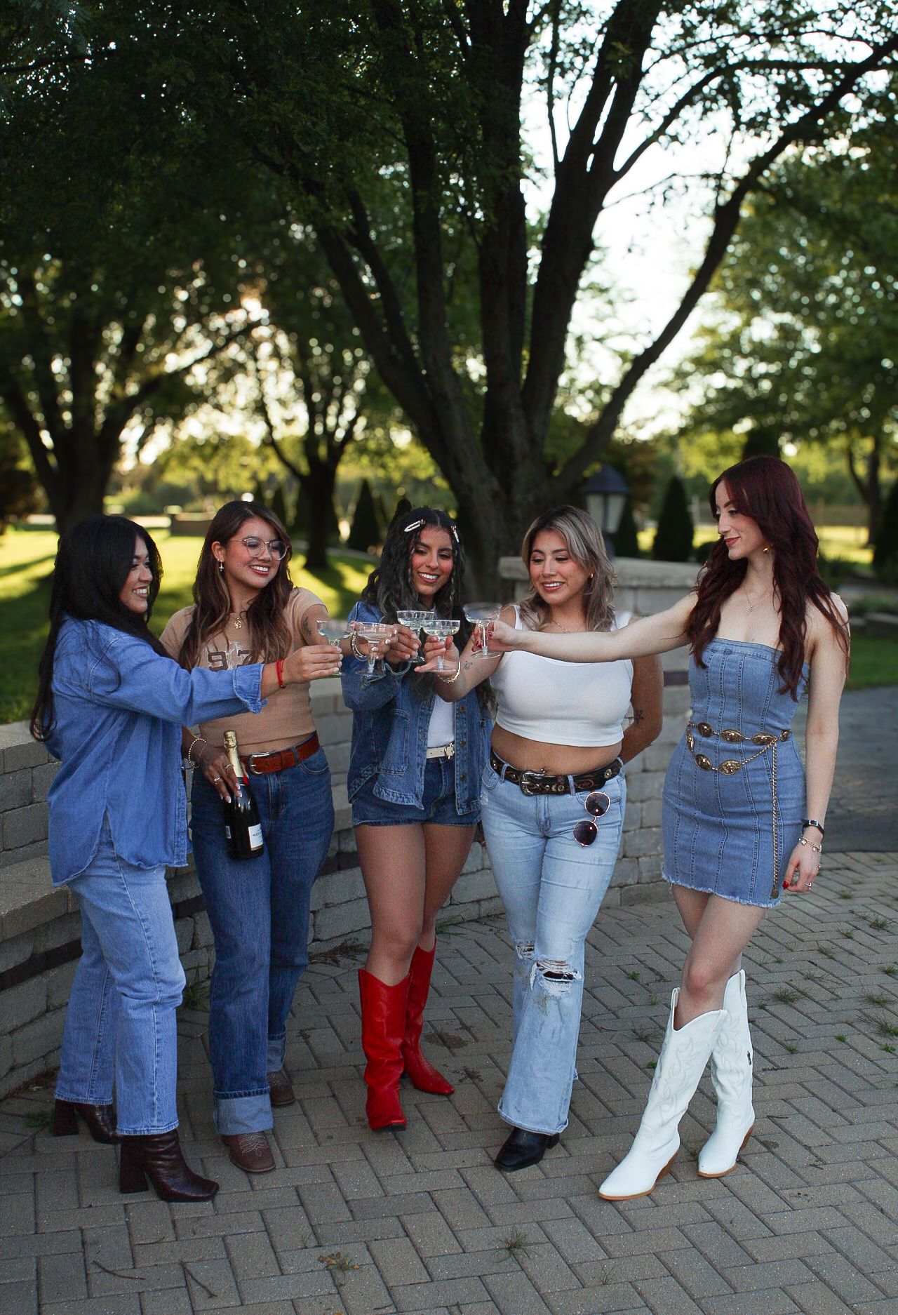 Group in western-inspired outfits with boots and denim gather on brick path during sunset.