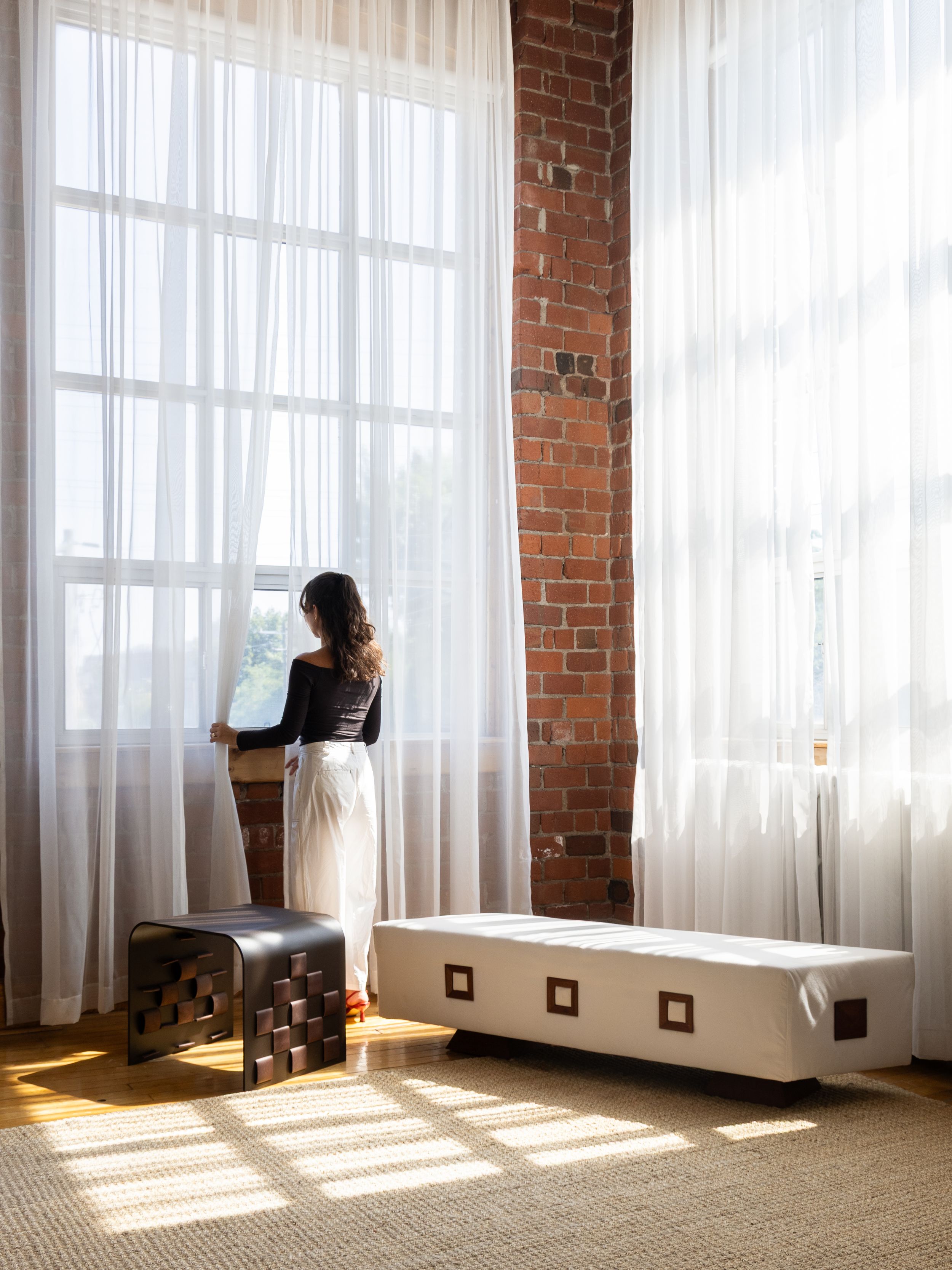 Sunlight streams through sheer white curtains in an industrial loft space with exposed brick walls.