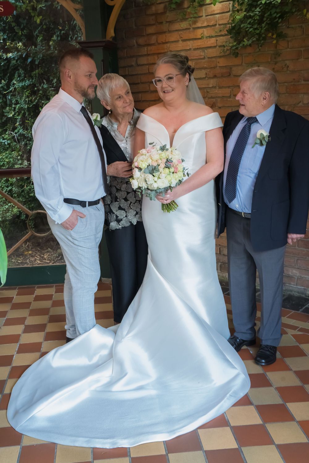 Couple dancing in white wedding attire on a checkered floor against a brick wall backdrop during their wedding celebration.
