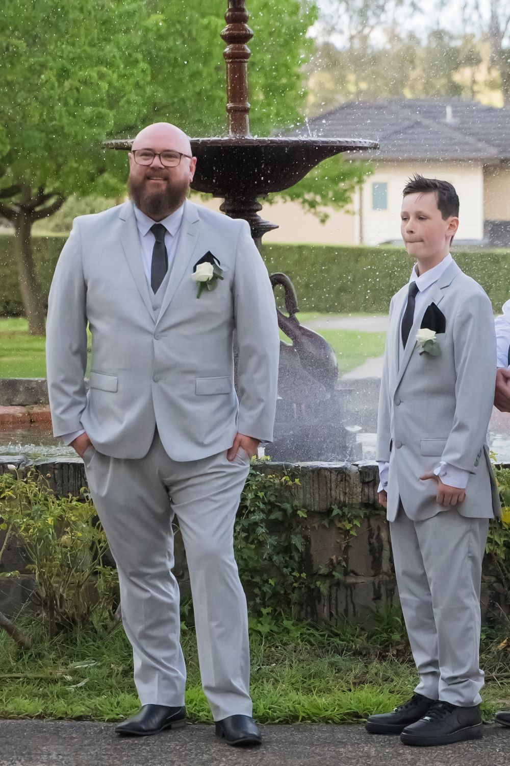 Groomsmen in light gray suits stand outside during a wedding photo session.