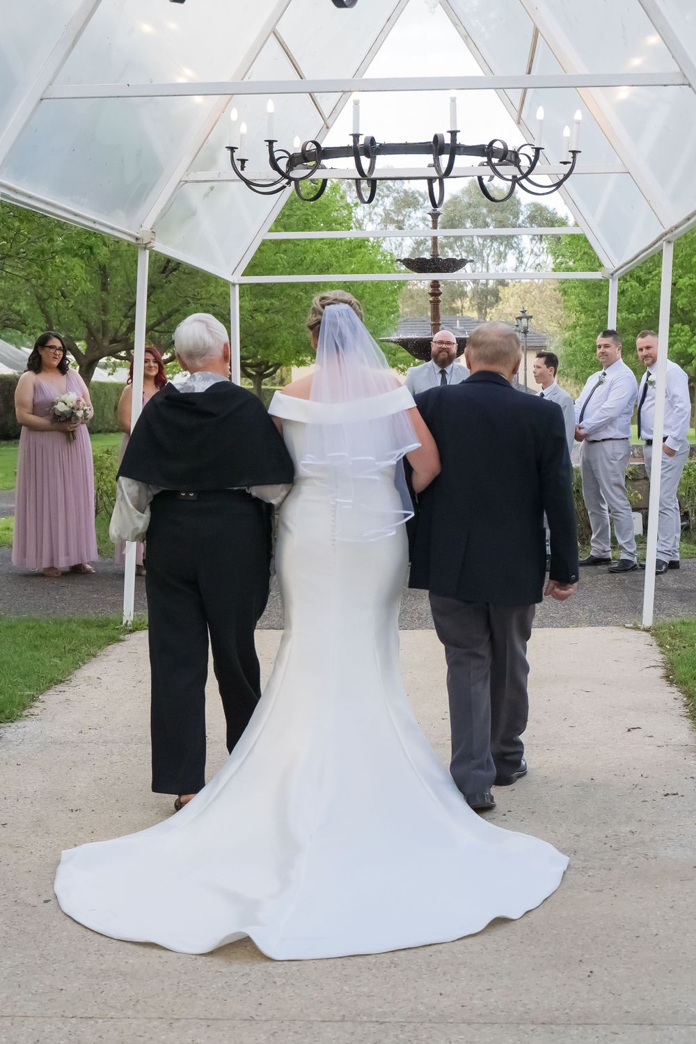 A series of wedding ceremony photos showing the back view of a bride in a stunning white gown with a flowing train.