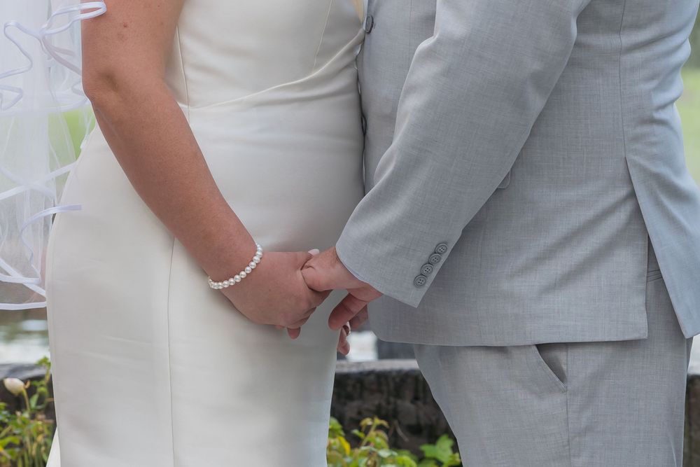 Couple holding hands at outdoor wedding ceremony while wearing light gray suits and suits.