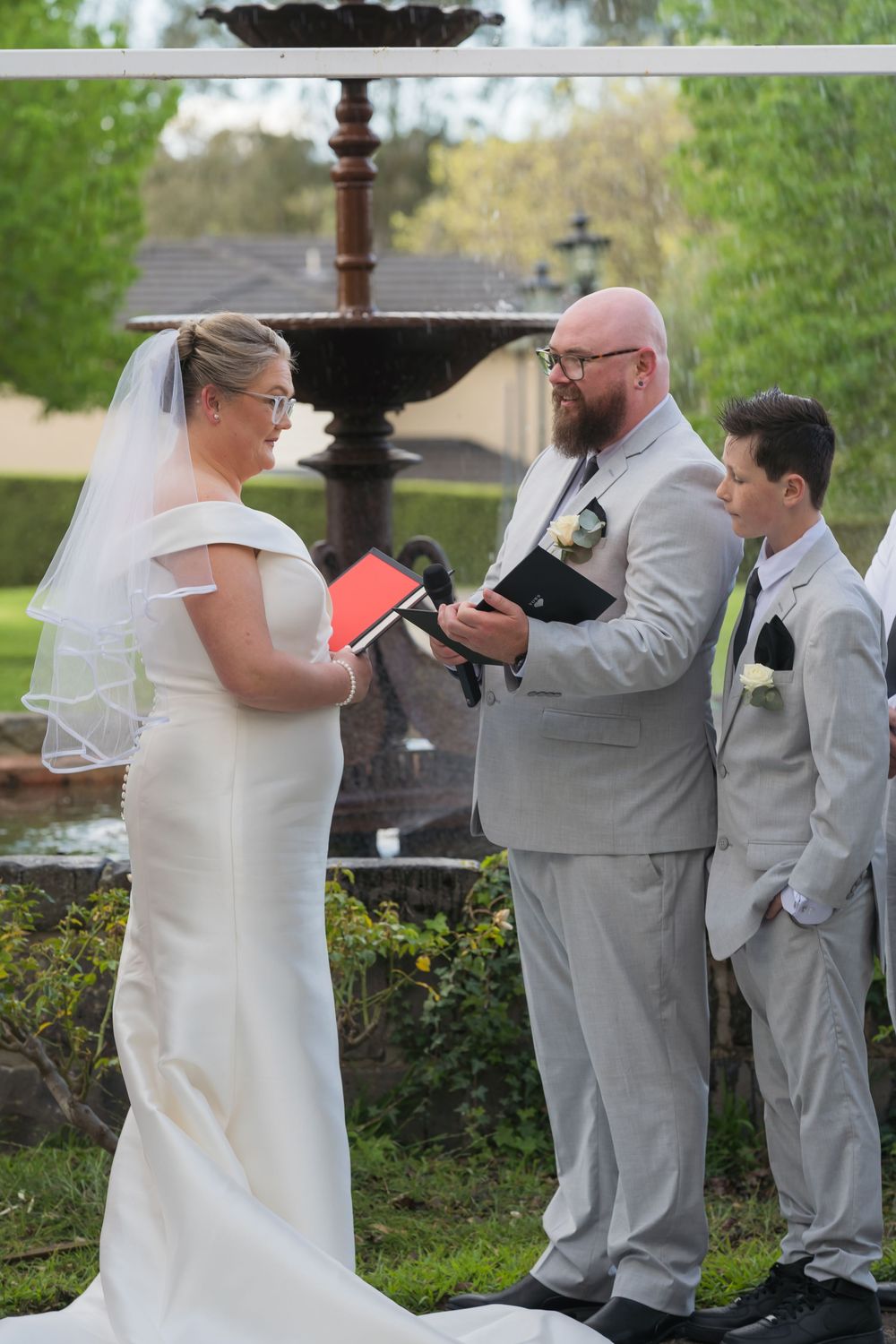 A wedding sequence shows a couple exchanging rings during an outdoor garden ceremony with attendants in light gray suits.