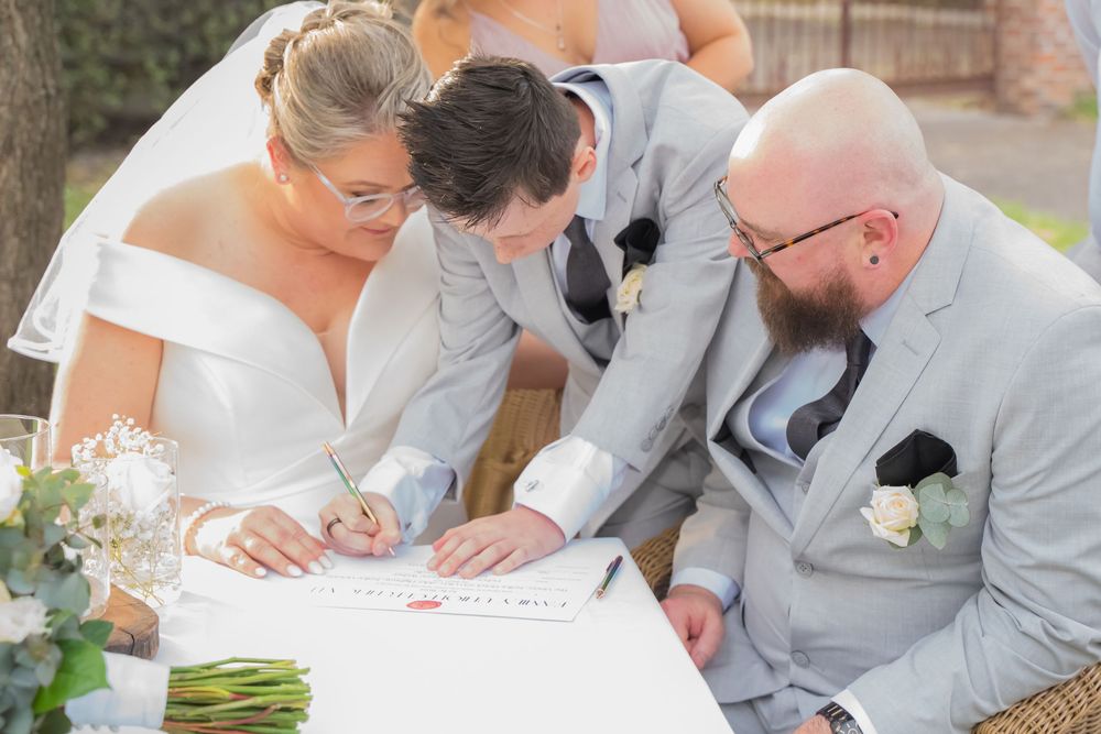 A couple signing wedding documents at a table while wearing matching gray wedding attire.