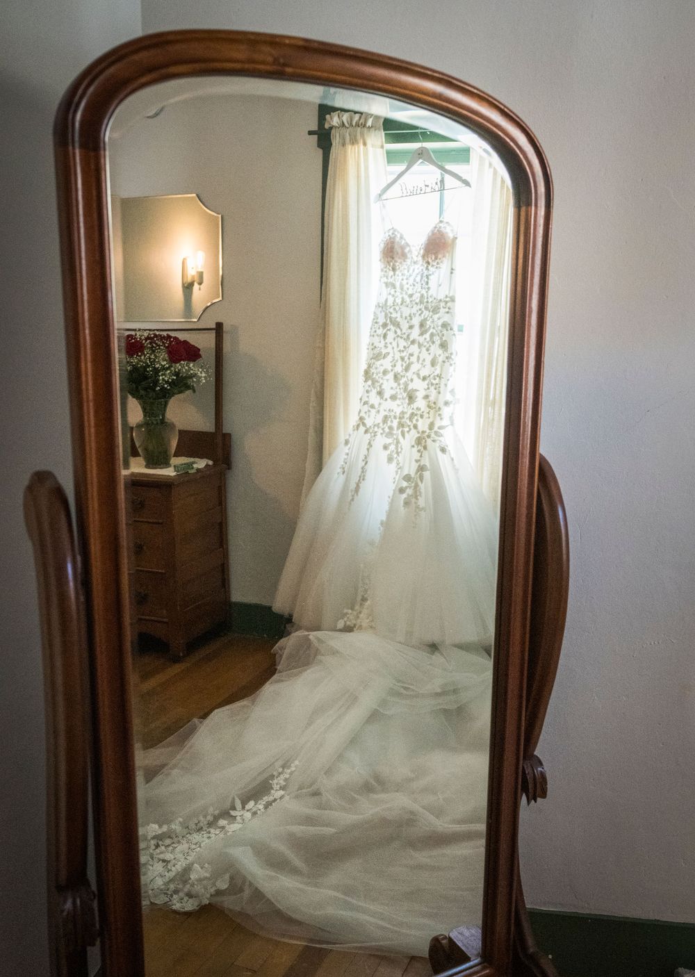 Wedding dress with long flowing train elegantly displayed in front of antique wooden mirror.