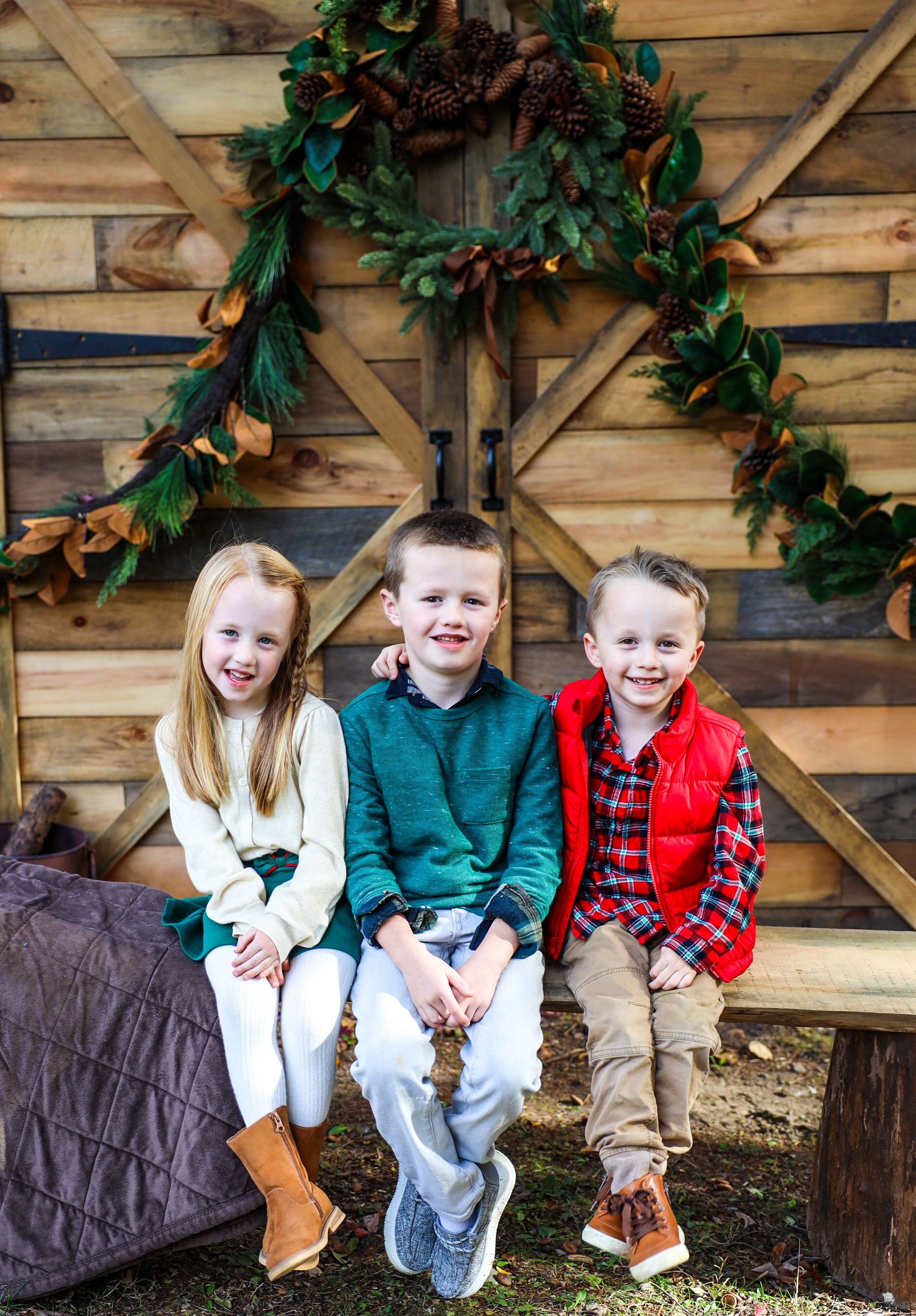 Children sitting together on wooden steps decorated with holiday greenery.