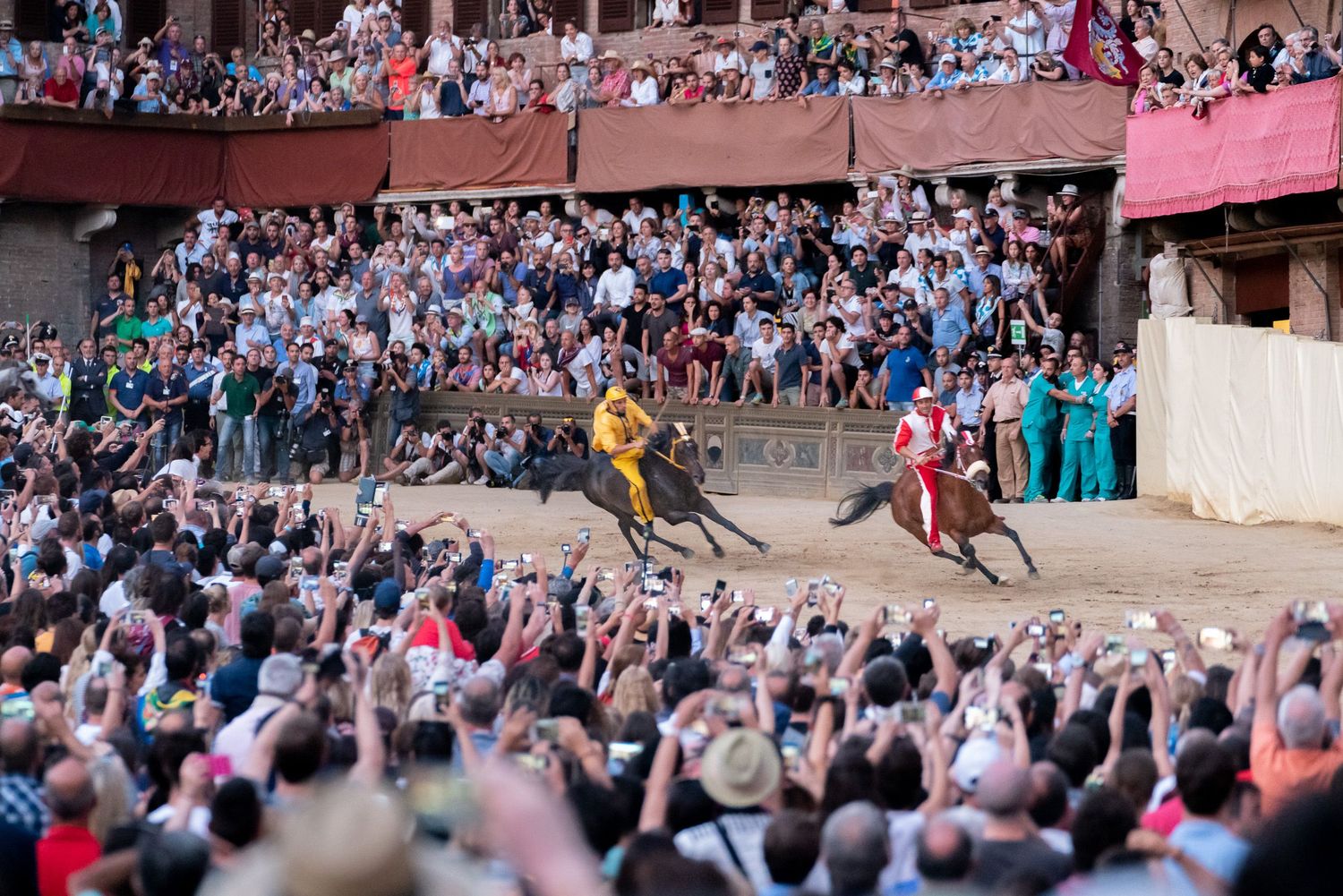 Spectators crowd stadium bleachers to watch horseback riders compete in a traditional racing event on dirt track.