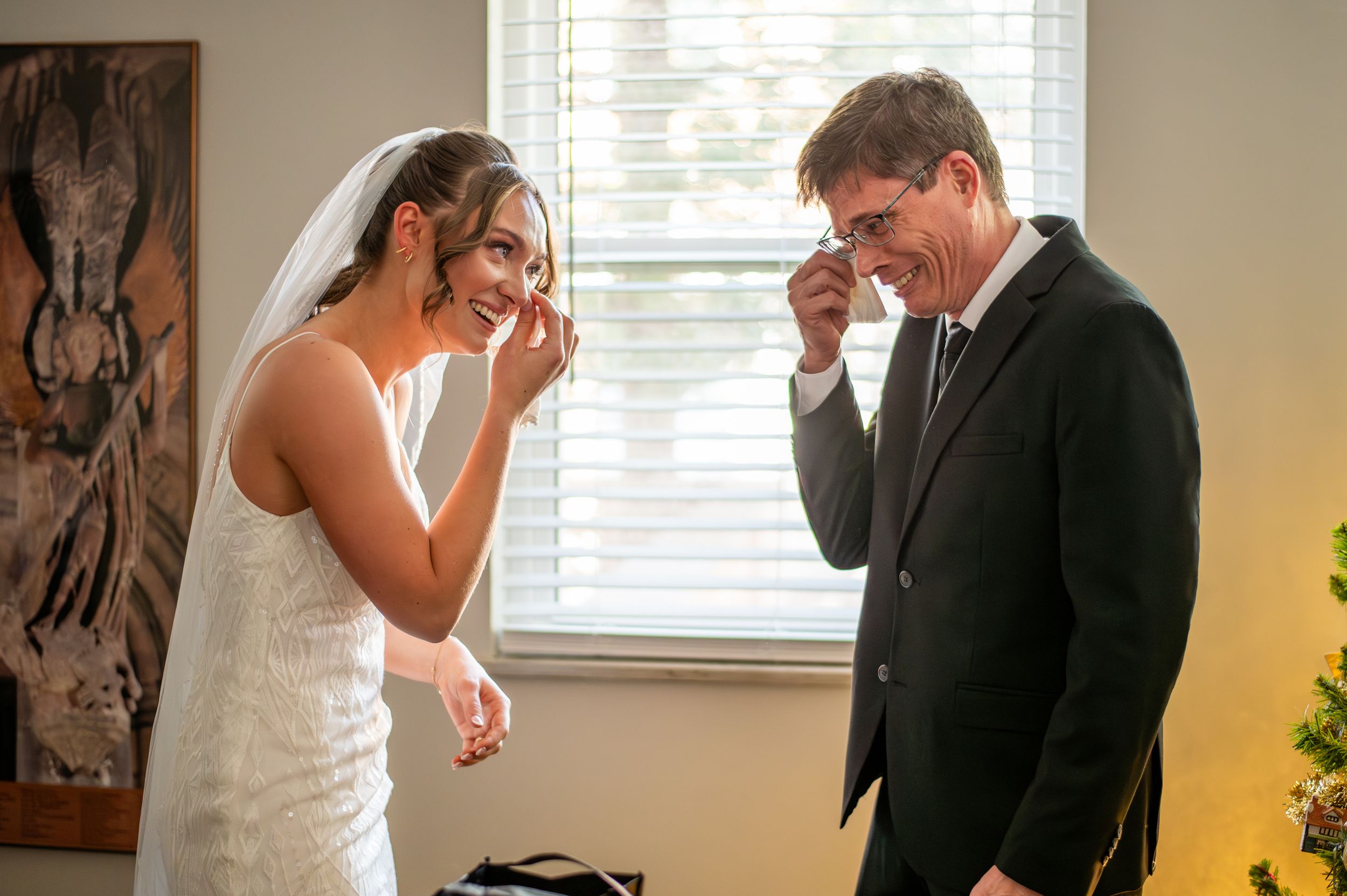 Two people in formal wedding attire share an emotional moment while laughing together indoors.