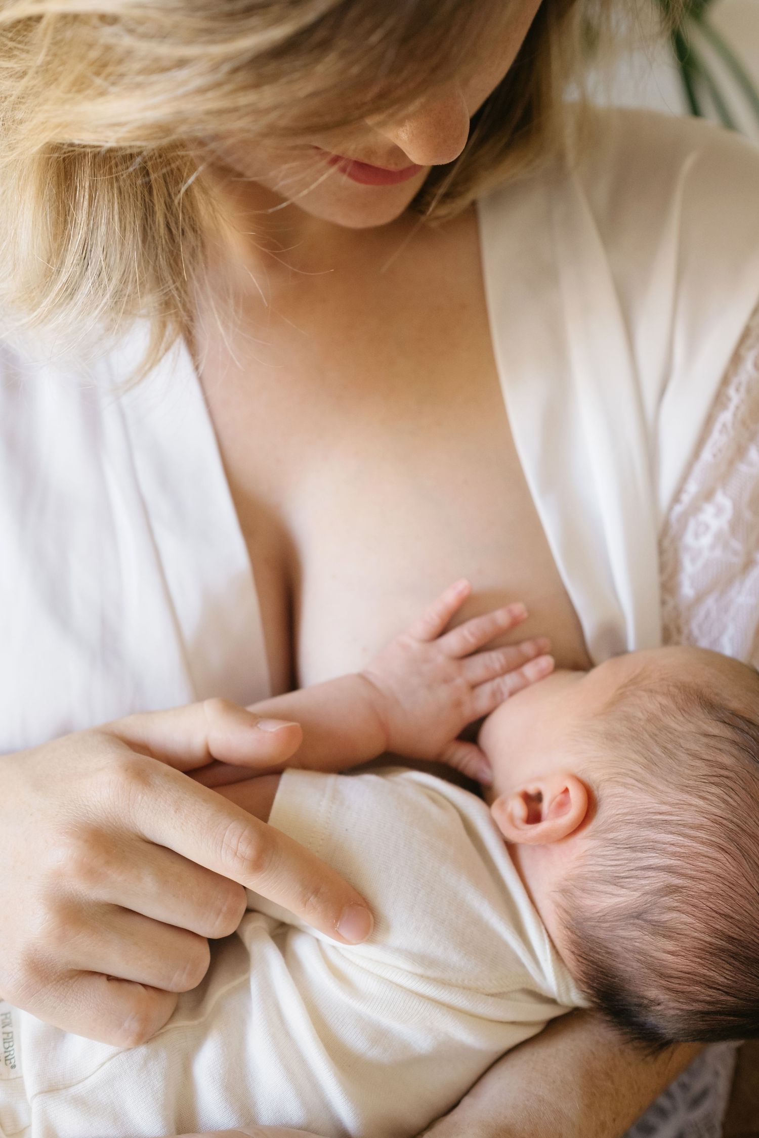 Tierno momento de madre dando pecho a su bebé lactante vestidos de blanco durante su sesión de fotografía newborn