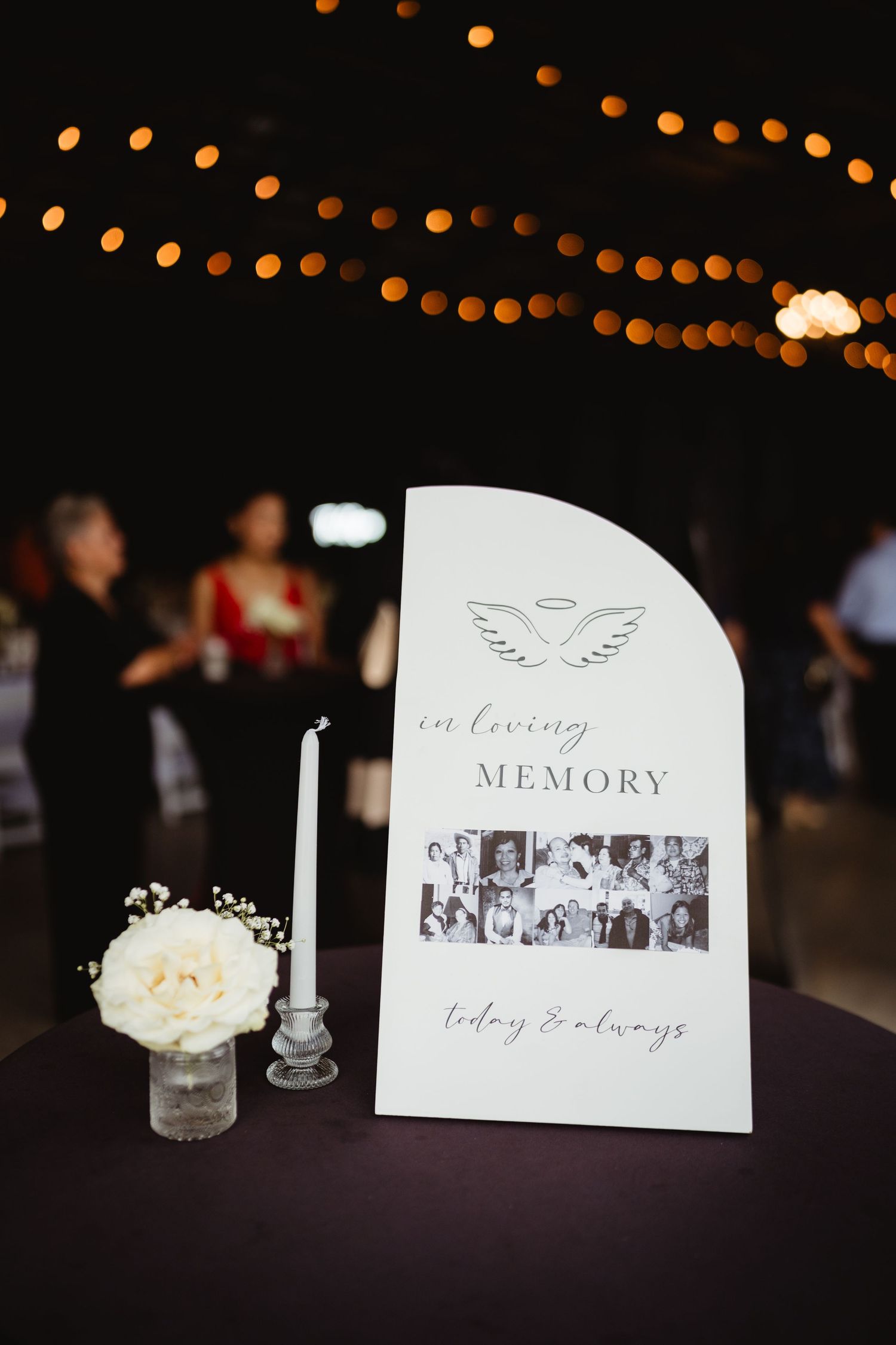 Memory table at evening wedding reception with string lights and photo displays of cherished moments.