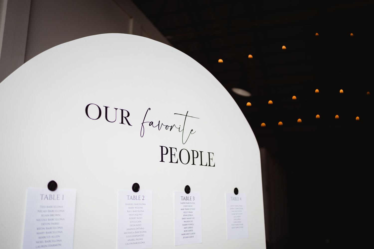 A wedding seating chart display with 'OUR favorite PEOPLE' written in elegant text against a white curved surface.
