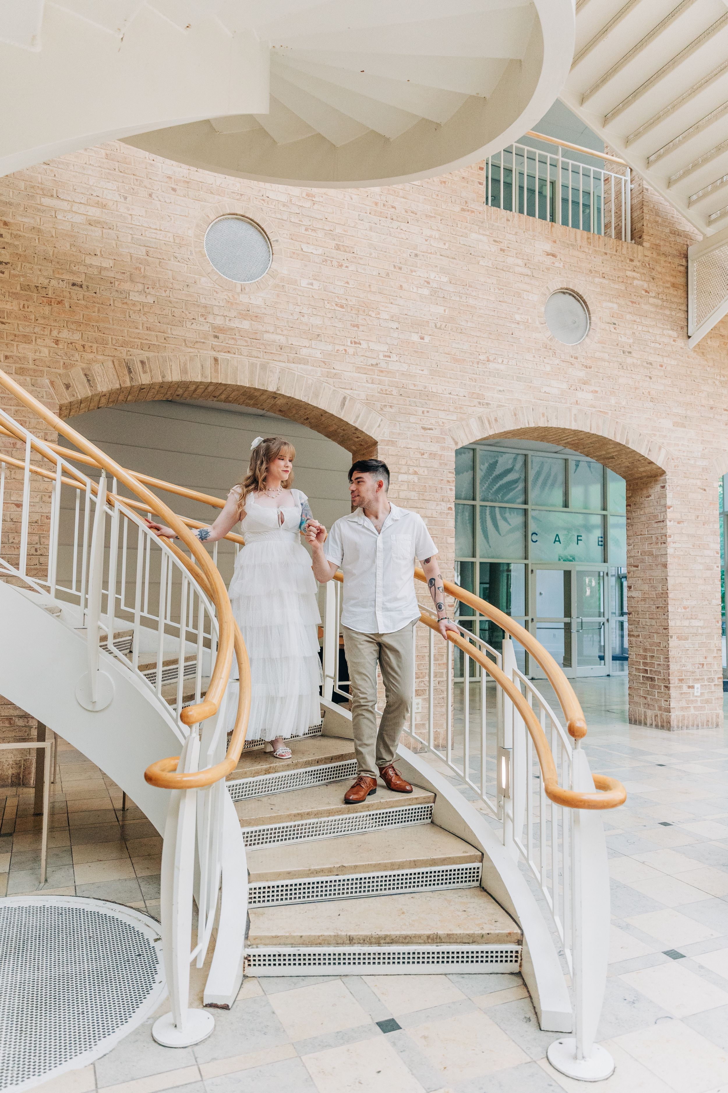 Elegant architectural interior features curved staircase with white railings and exposed brick walls in modern building.