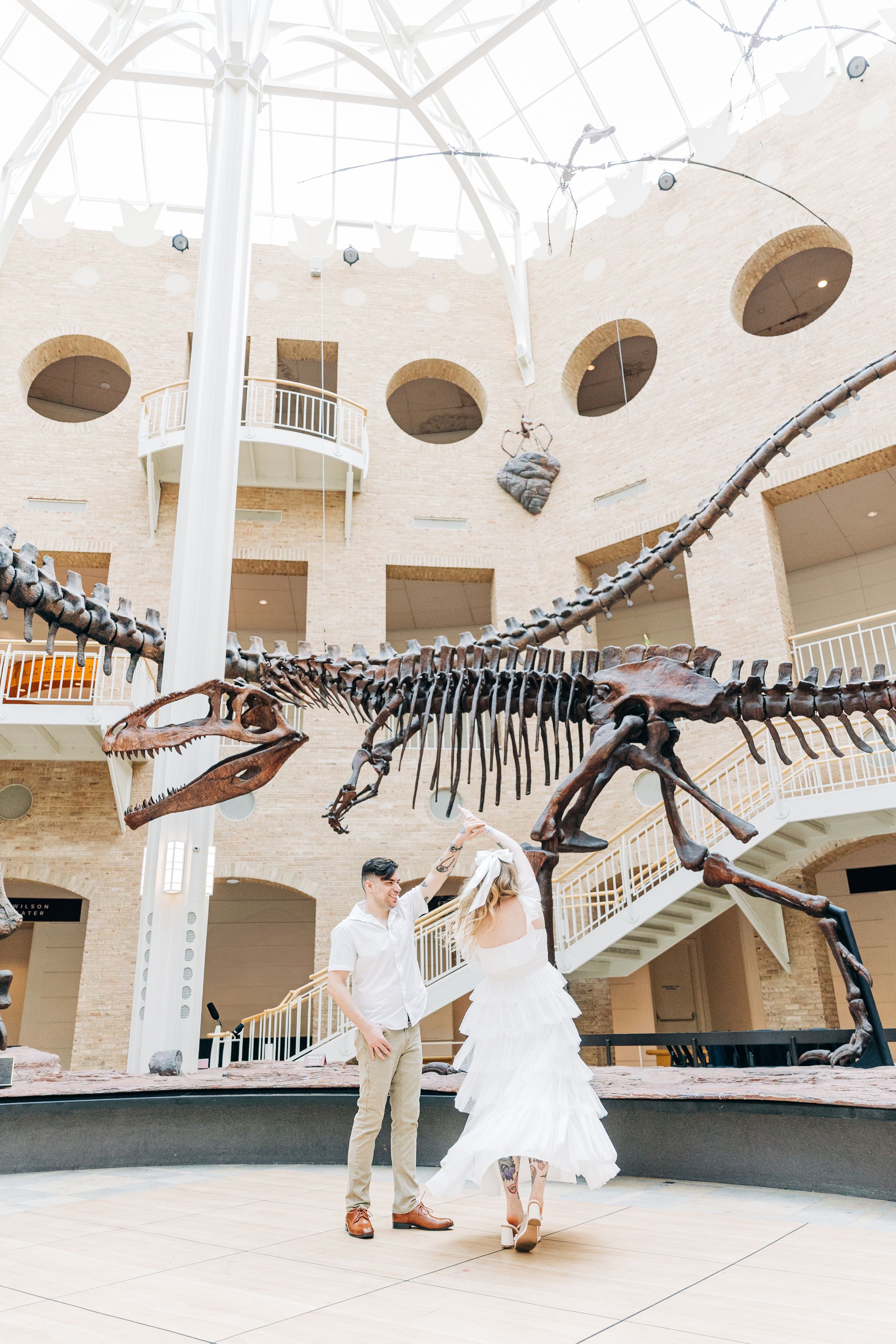 A couple takes wedding photos in front of a large dinosaur skeleton display at a natural history museum.