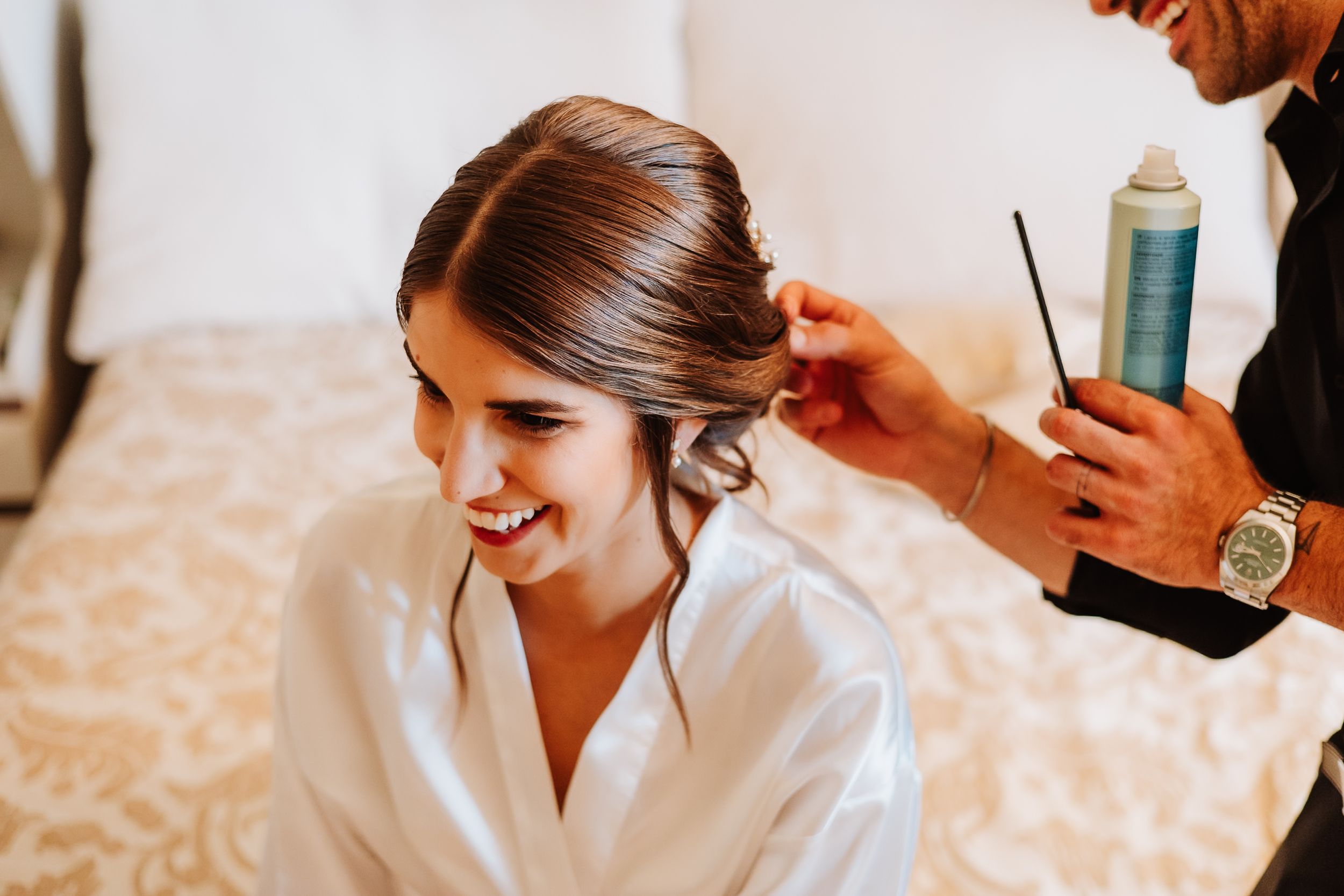Hair stylist working on an elegant bridal updo during wedding day preparations.