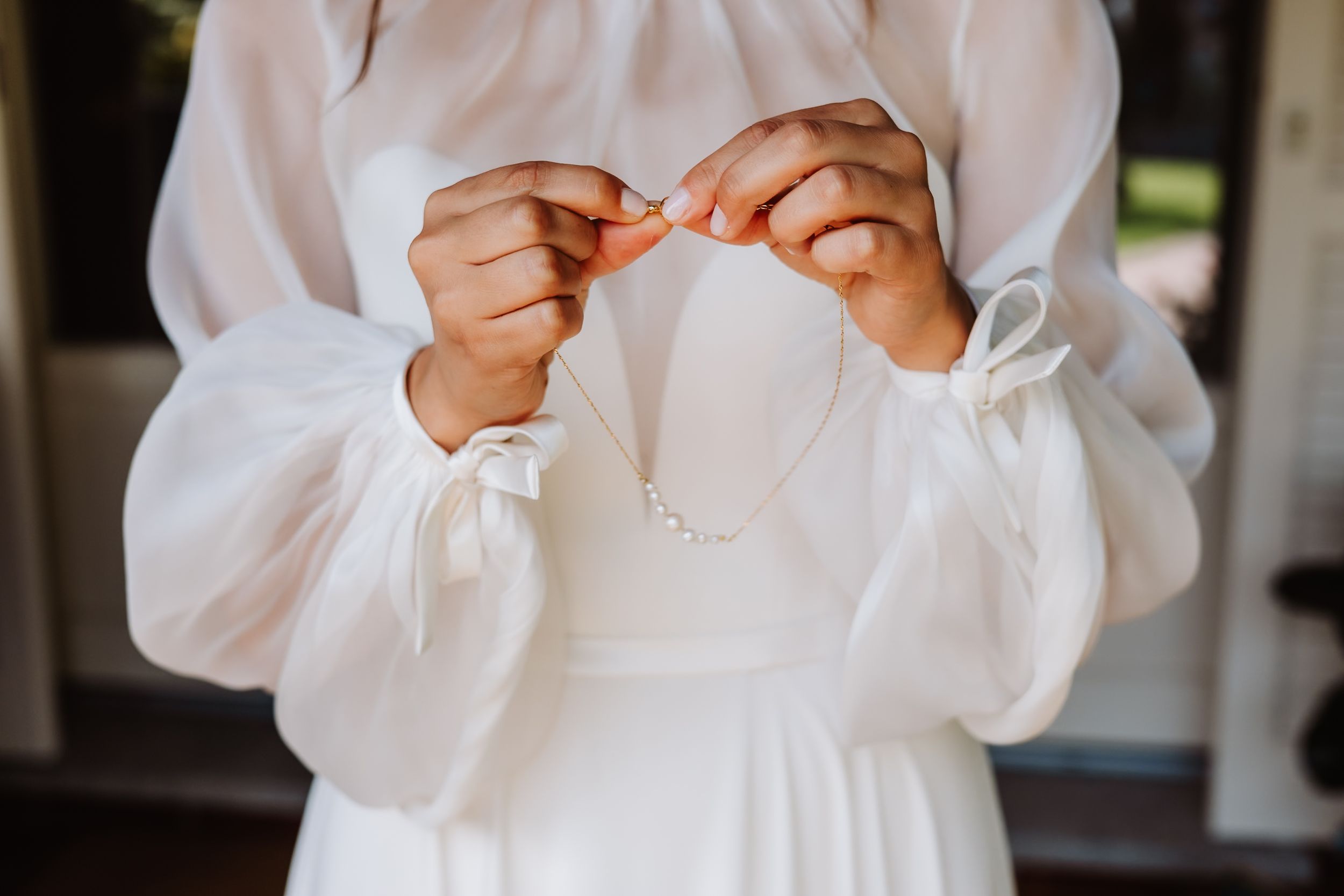 Close-up view of hands adjusting details on a crisp white long-sleeved dress.