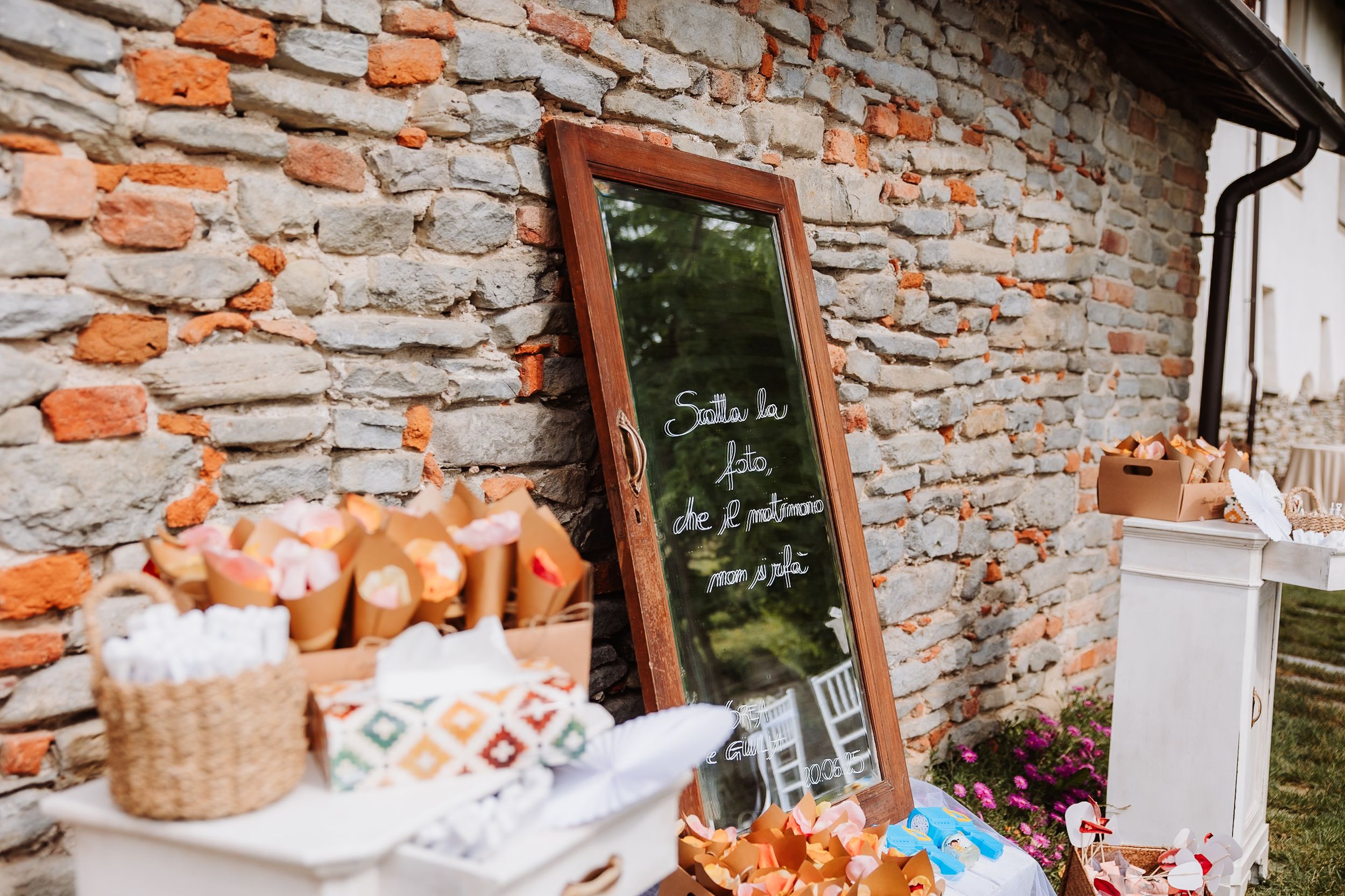 A rustic outdoor party setup with a mirror chalkboard menu against a brick wall near food and drink displays.