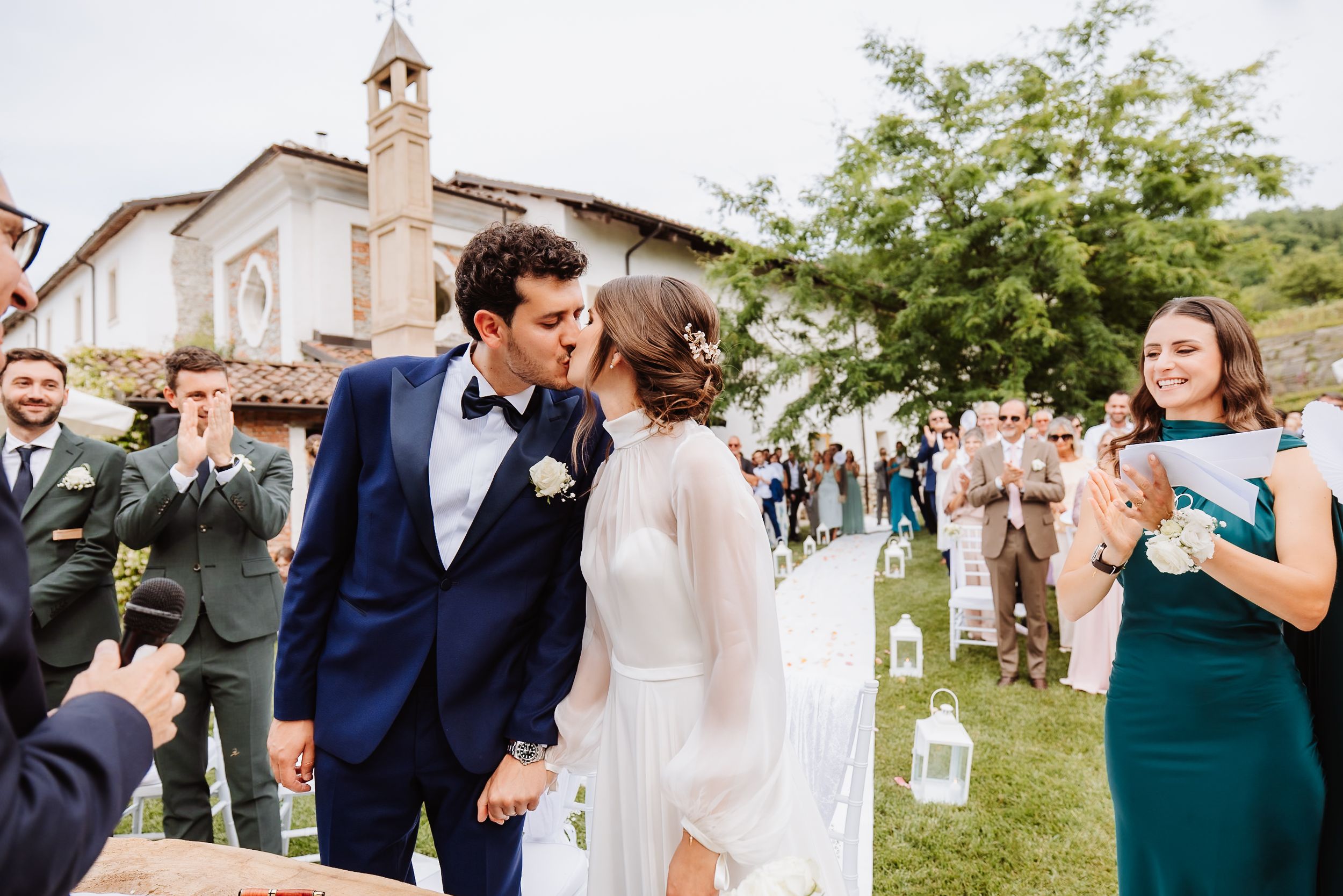 A blissful wedding celebration unfolds at an outdoor garden venue with guests dressed in formal attire.