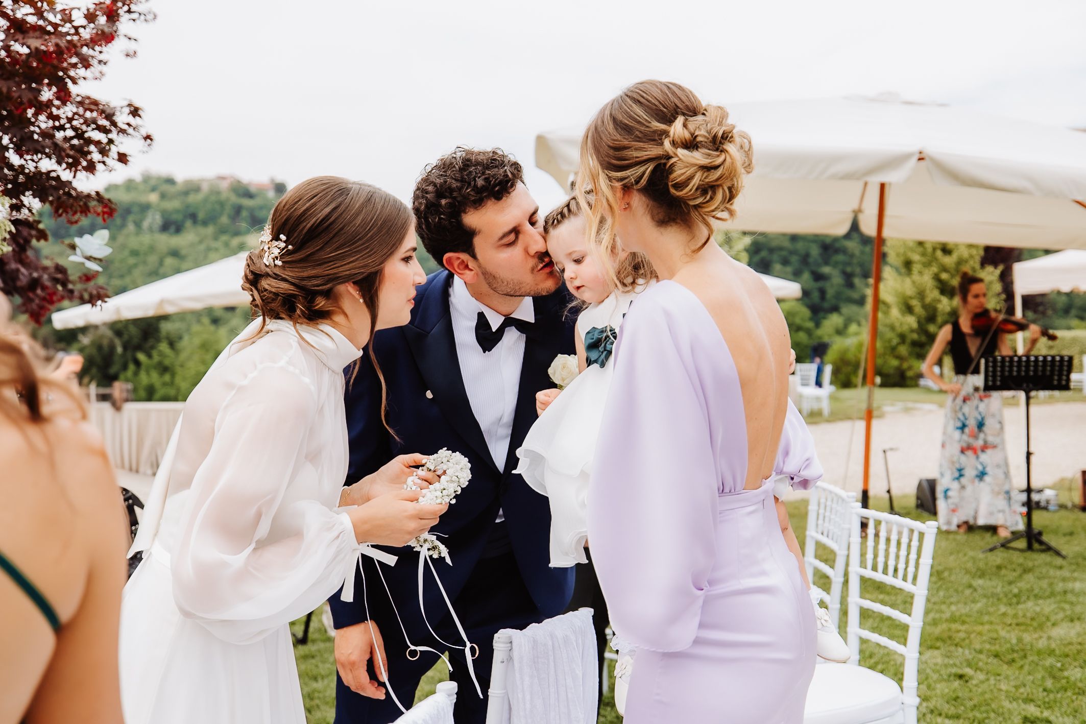 People sharing an intimate moment at an outdoor garden wedding reception with white chairs and umbrellas in background.
